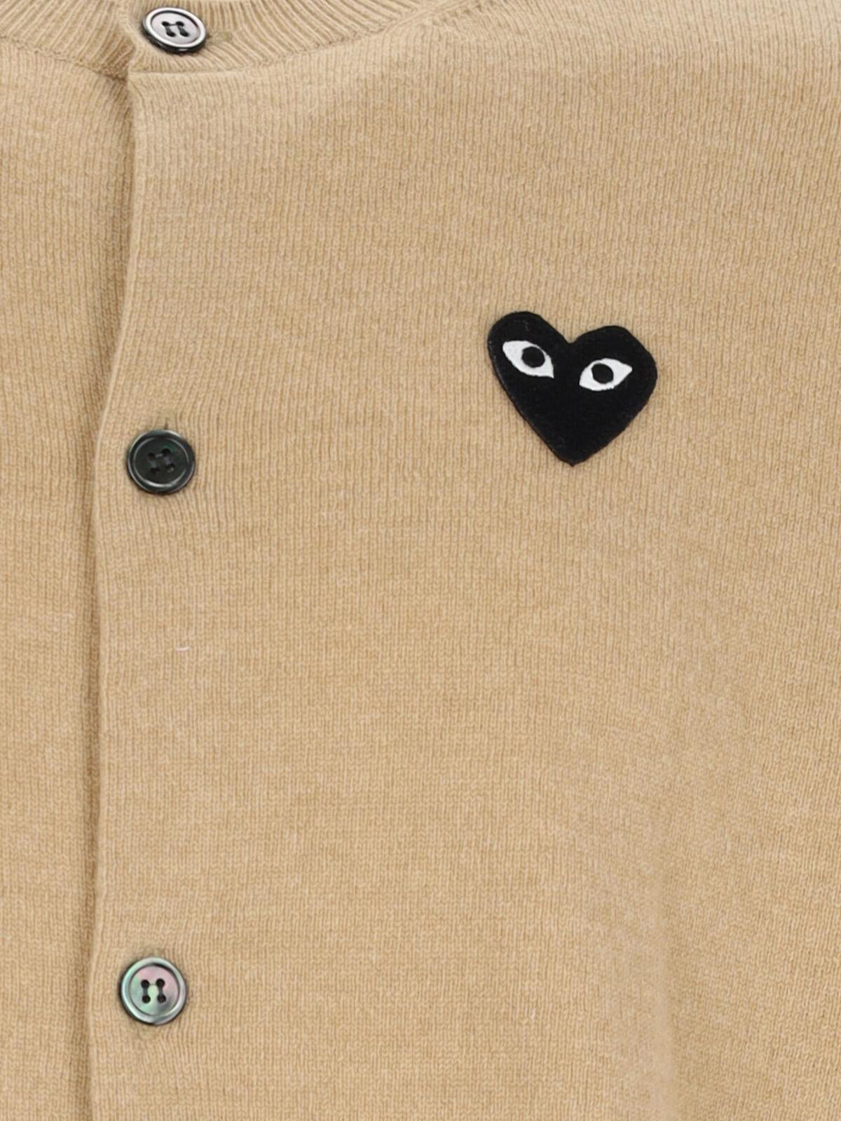 1. Close-up of COMME des GARÇONS PLAY black heart emblem and button fastening on Light Camel knit