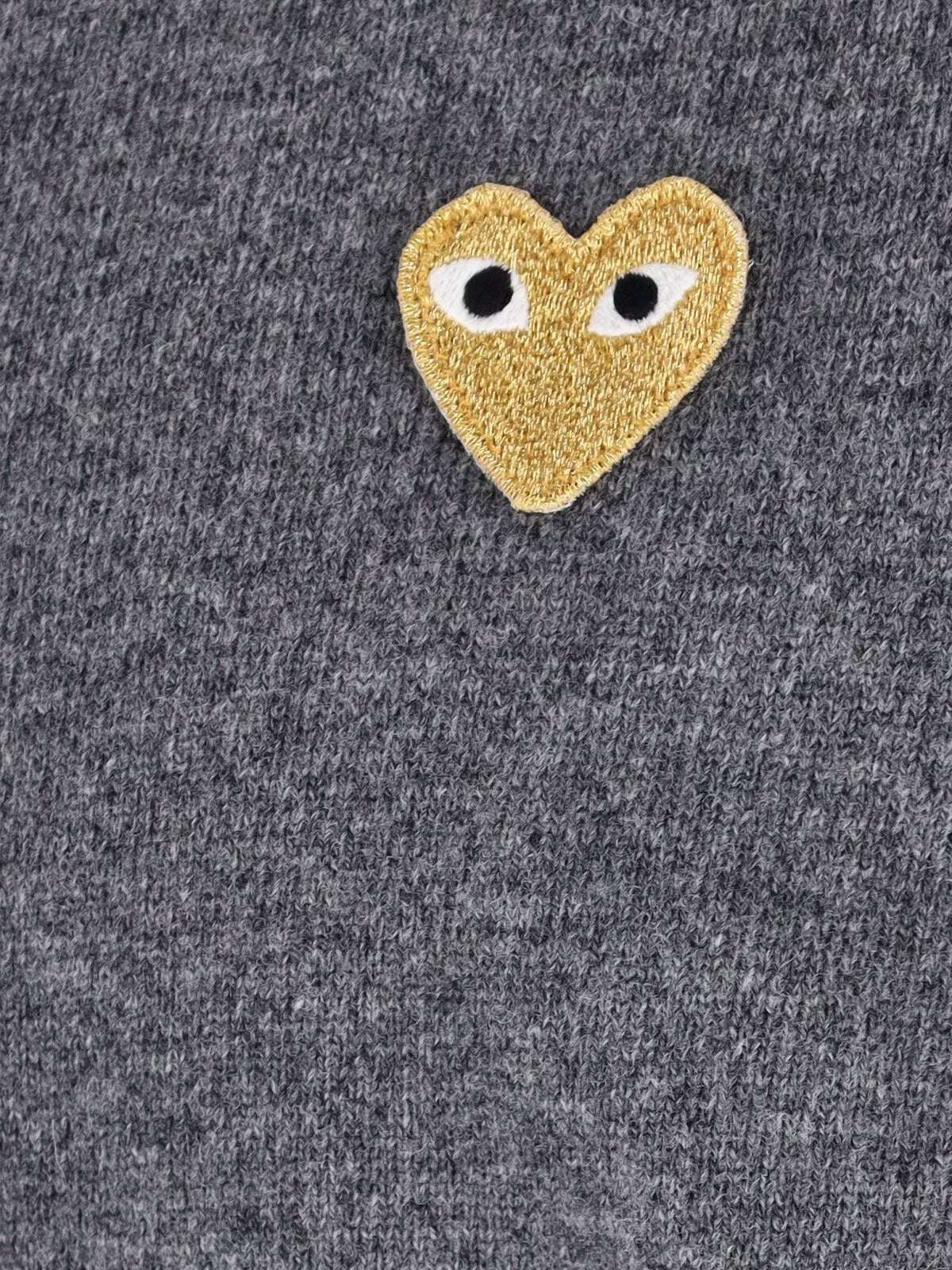 Close-up of COMME des GARÇONS PLAY medium grey wool cardigan showing the textured knit and signature gold heart emblem with white eyes