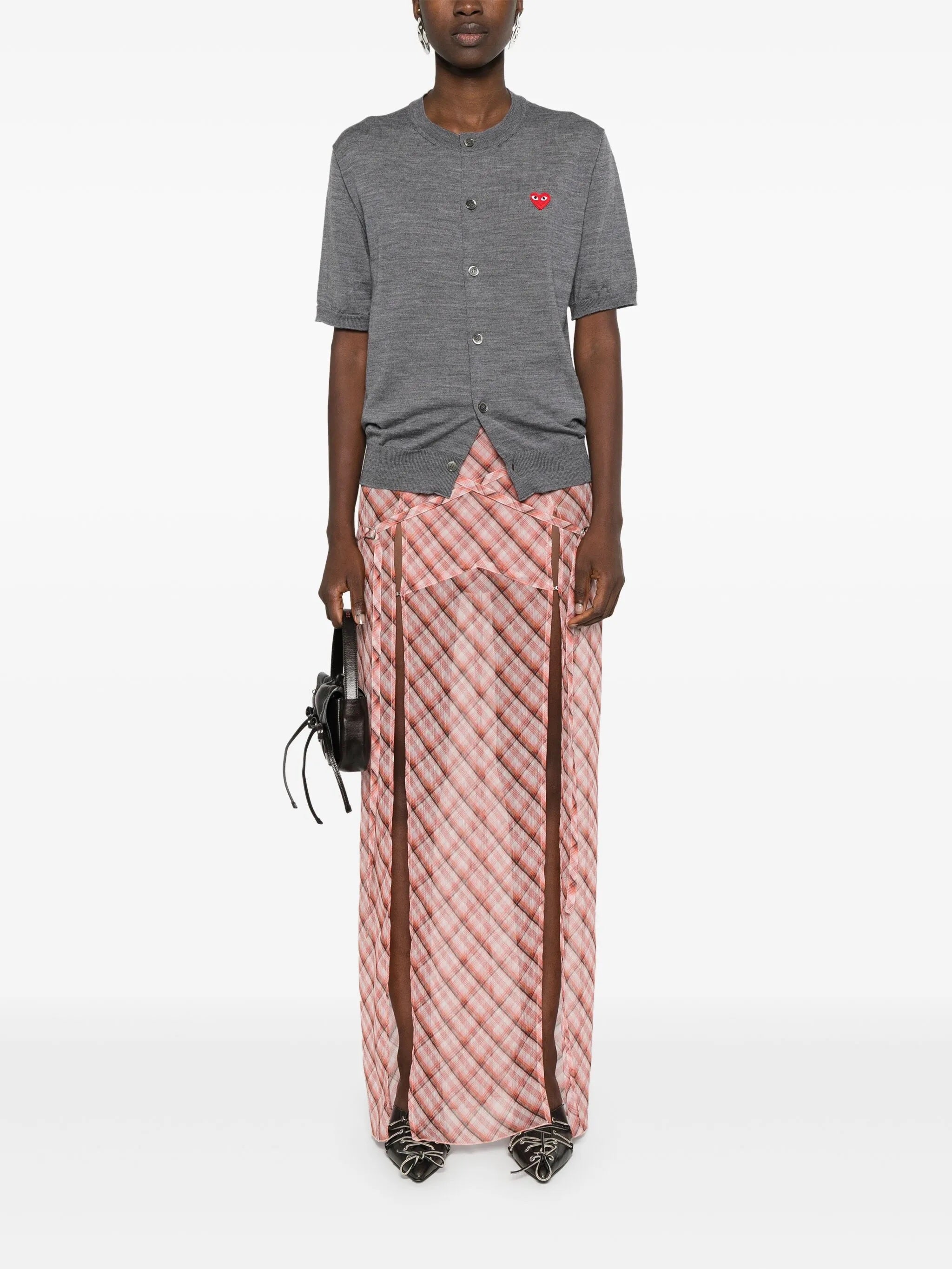 Female model wearing the short-sleeve cardigan with a red heart logo from Comme des Garcons Play on a white background