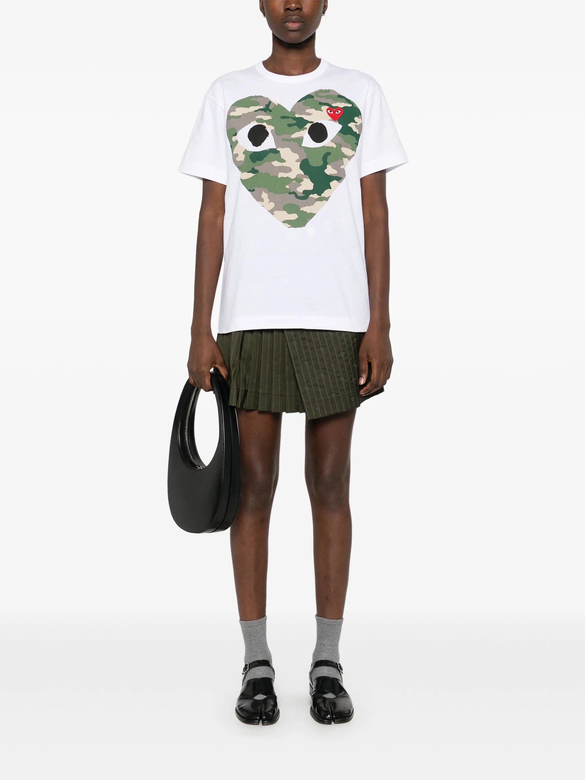 Model wearing Comme des Garçons Play Camouflage Shirt Red Heart in white with green heart print, short sleeves and unisex fit