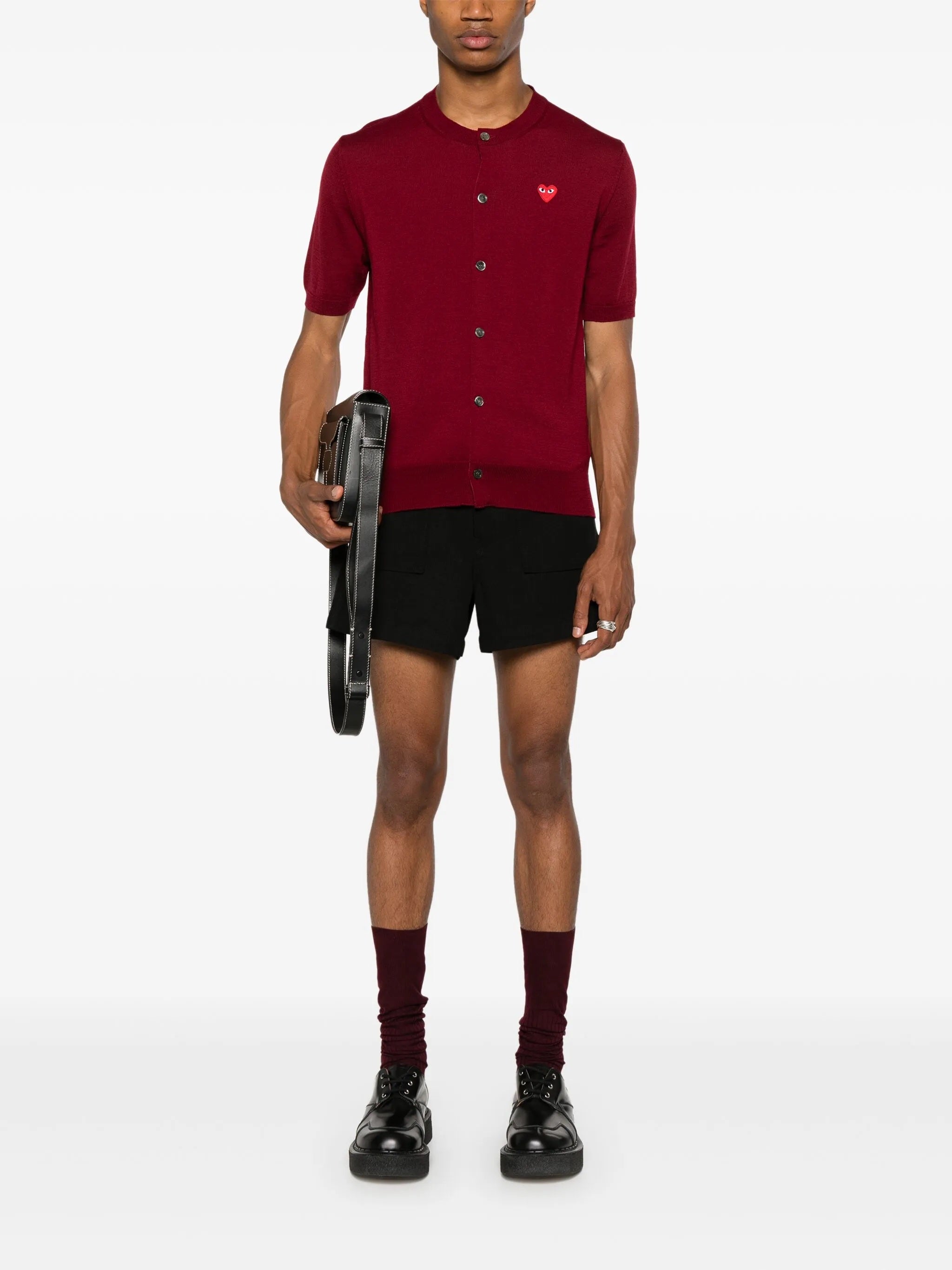 Male model wearing the red short-sleeve cardigan with a red heart logo from Comme des Garcons Play on a white background