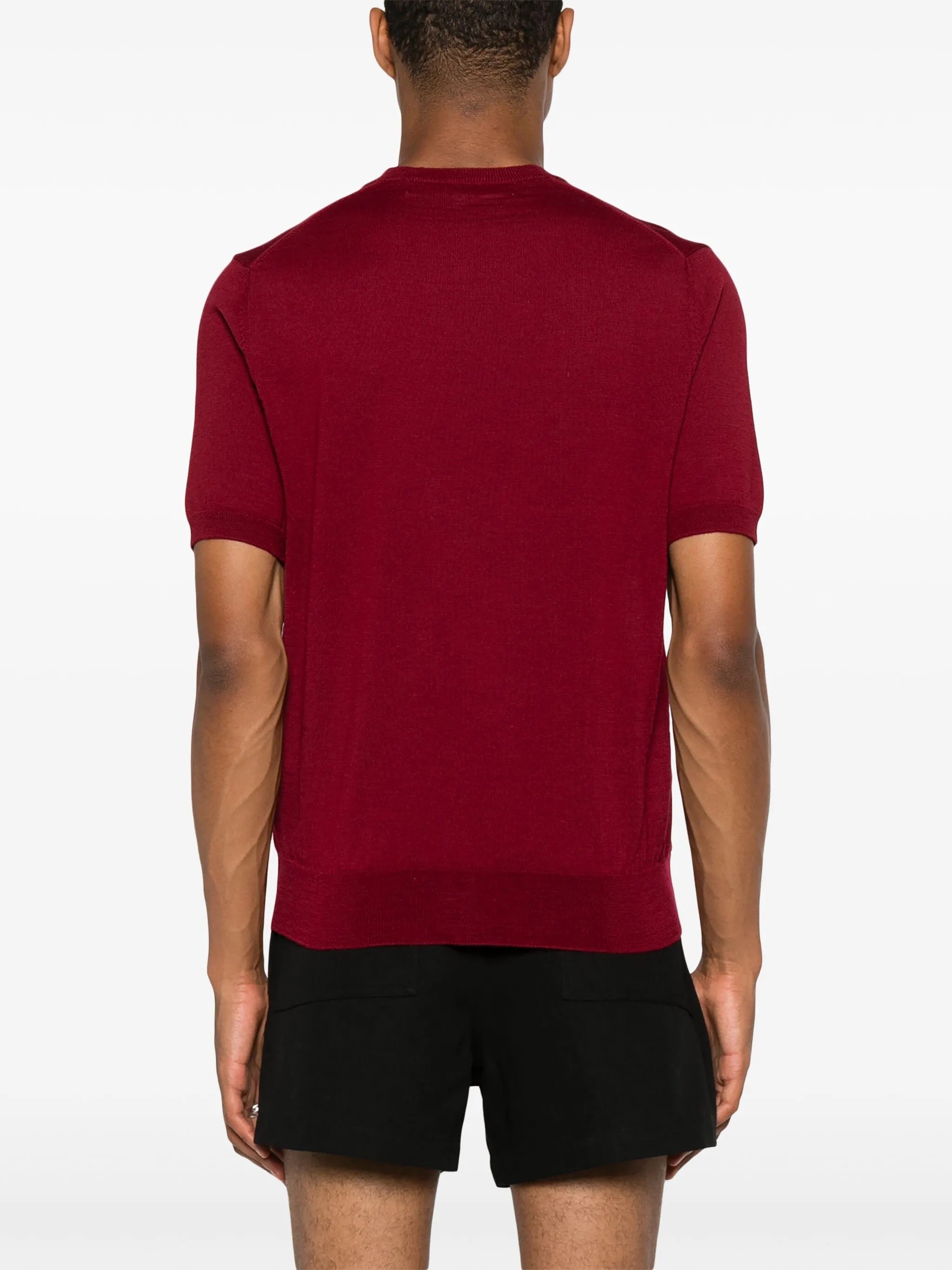 Back profile of male model wearing the red short-sleeve cardigan with a red heart logo from Comme des Garcons Play on a white background