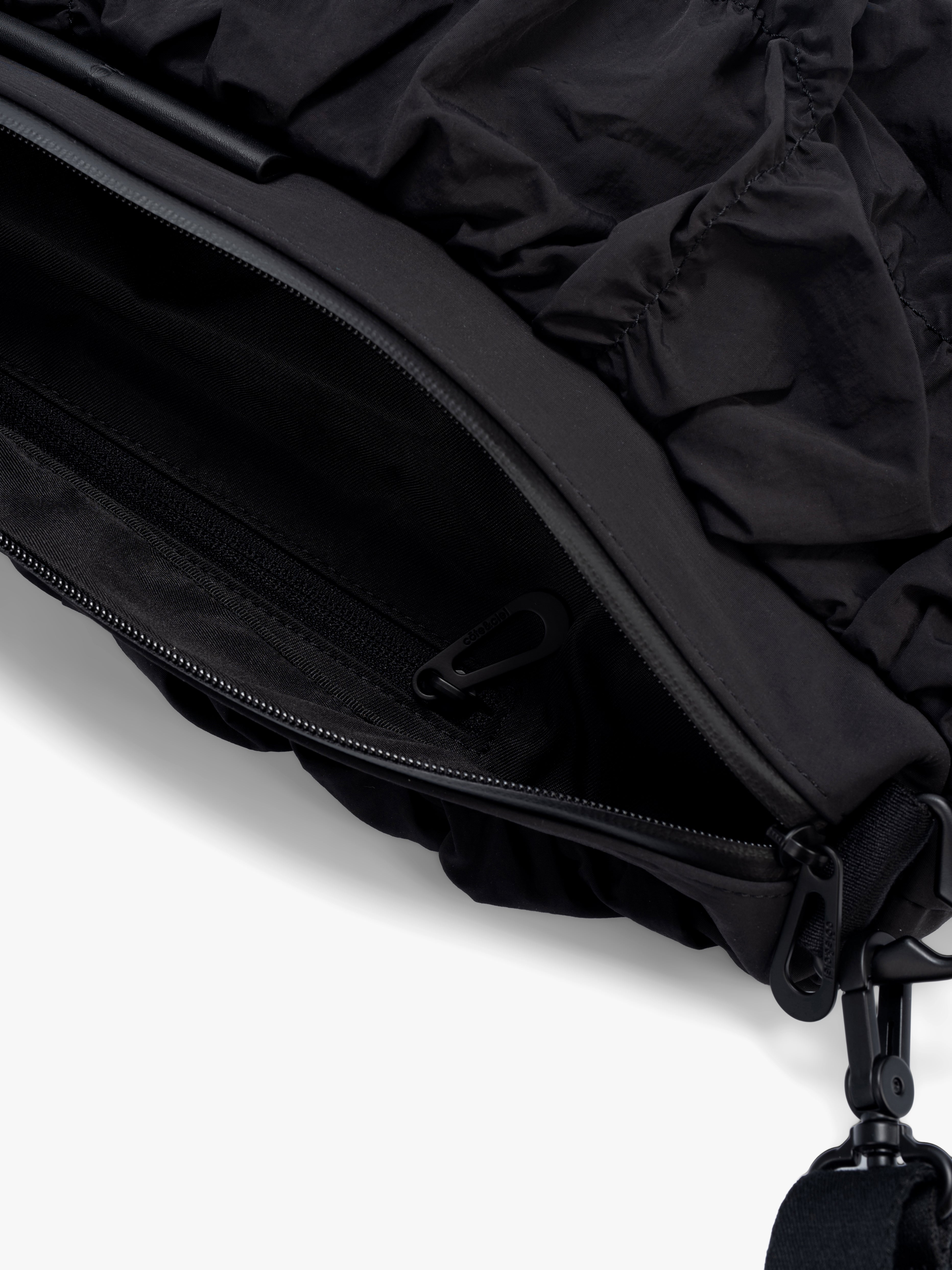 Closeup of Côte&Ciel Orne Otra Gathered black bag with zipper open, showing secure interior compartment and textured nylon construction.