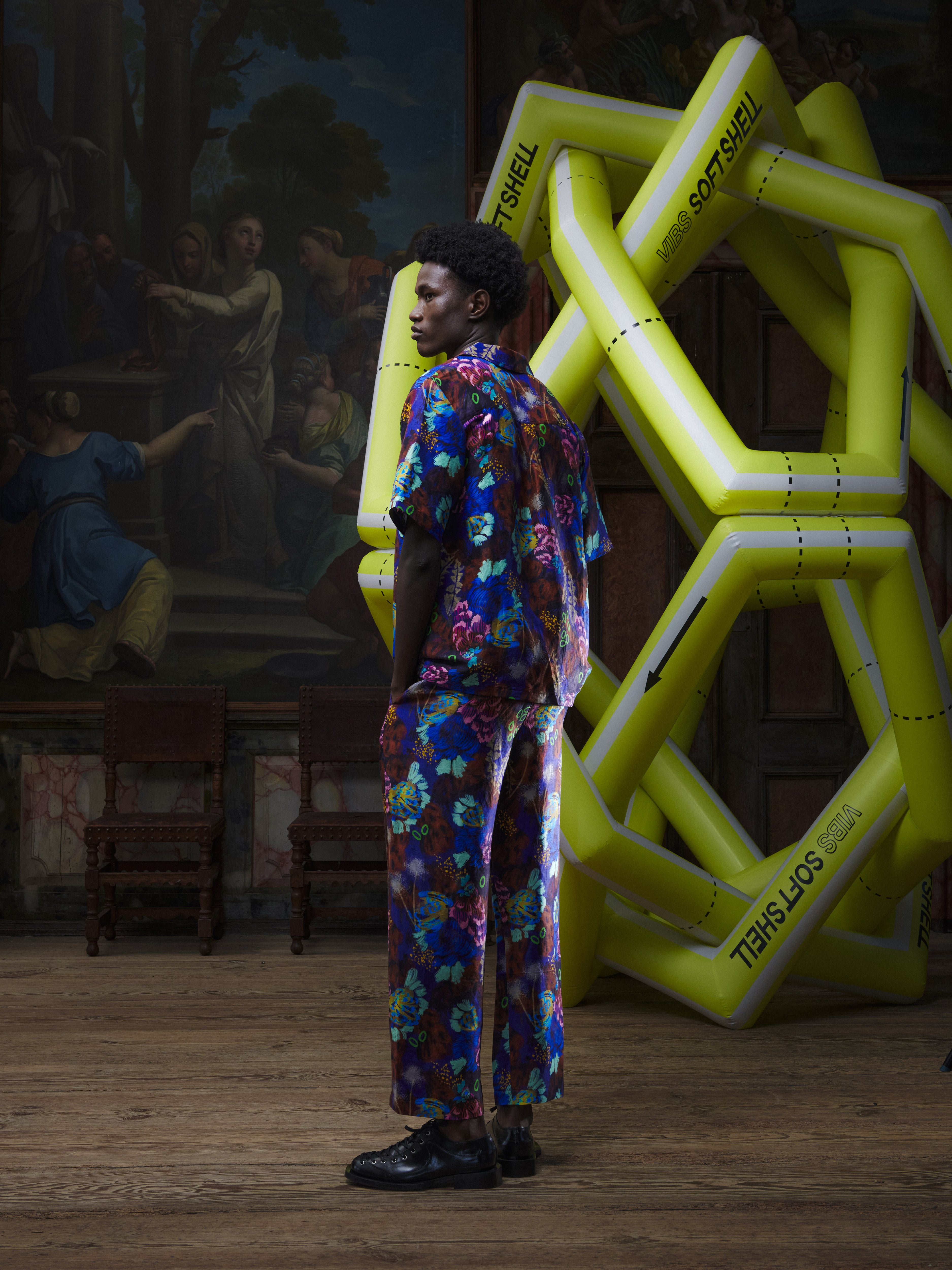 Back view of the male model wearing the Artist Shirt in Space Chickens from Henrik Vibskov Spring/Summer 2026 Studio Collection, showing the full colourful print and straight hem.