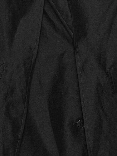 Close-up of the Beetle Coat showing the black fabric texture, layered construction, and curved hem detail.