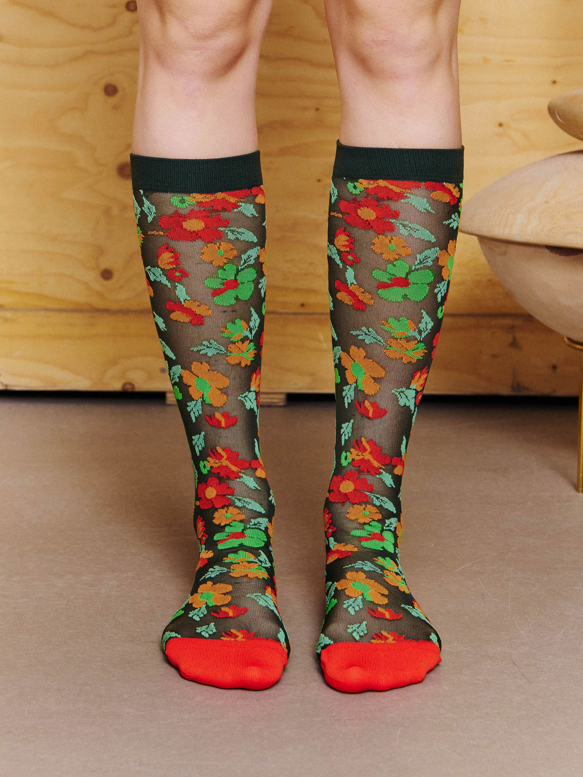 Front view of model wearing the Henrik Vibskov Bouquet Socks in Orange Floral Affairs, showing the semi-sheer floral pattern and mid-calf fit.