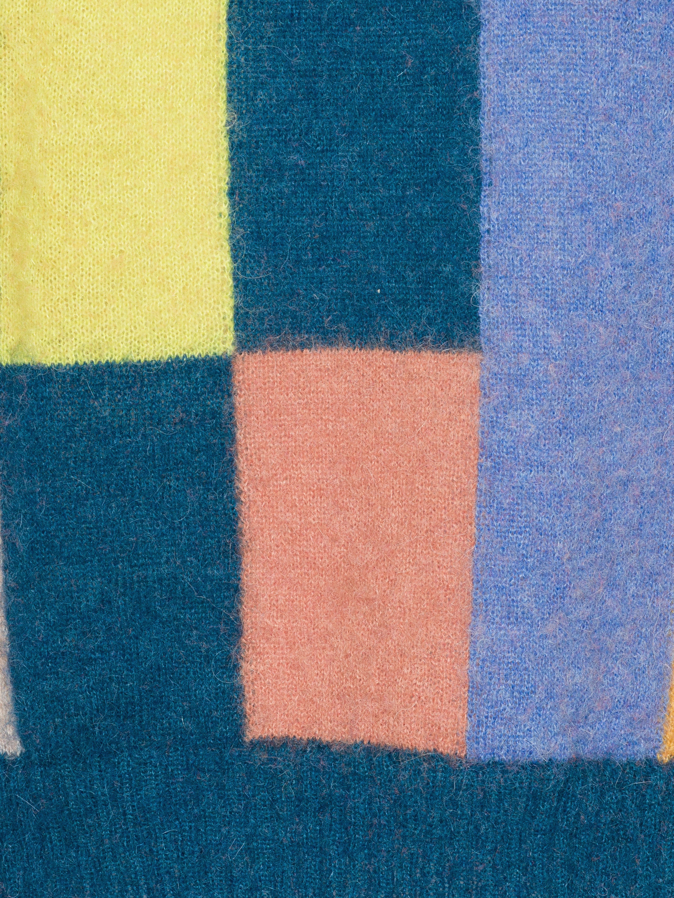 Close-up of a textured fabric with geometric color blocks in blue, yellow, and pink.