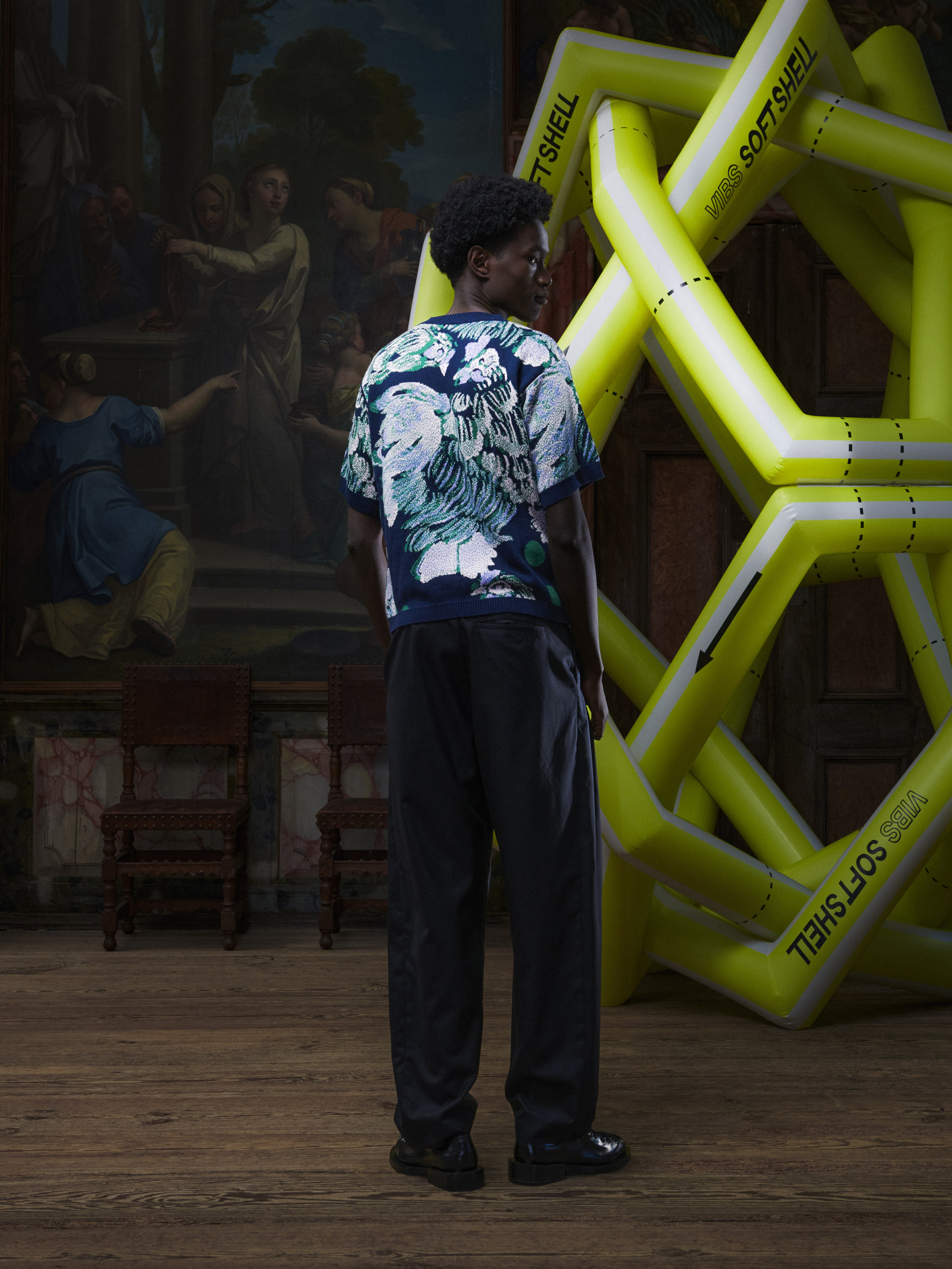 Back full-body view of the male model wearing the Chicken T Knit in Chicken Navy from Henrik Vibskov Spring/Summer 2026 Studio Collection, showing the straight hem and short-sleeved navy knit.