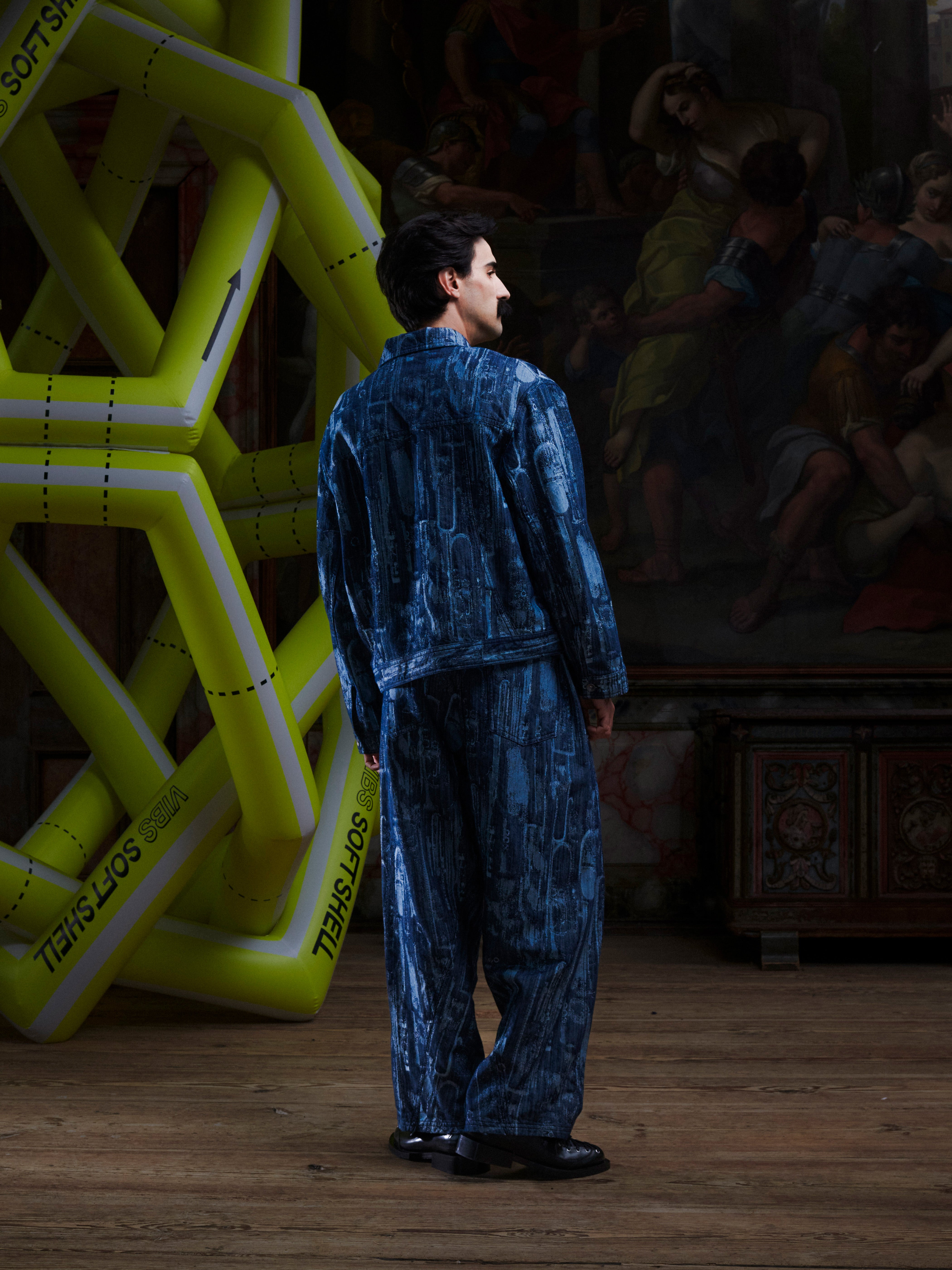Back view of the male model wearing the Curved Denim Pants, showing the back pockets, straight-leg cut, and abstract pattern. Model is 185cm tall and wears size M.