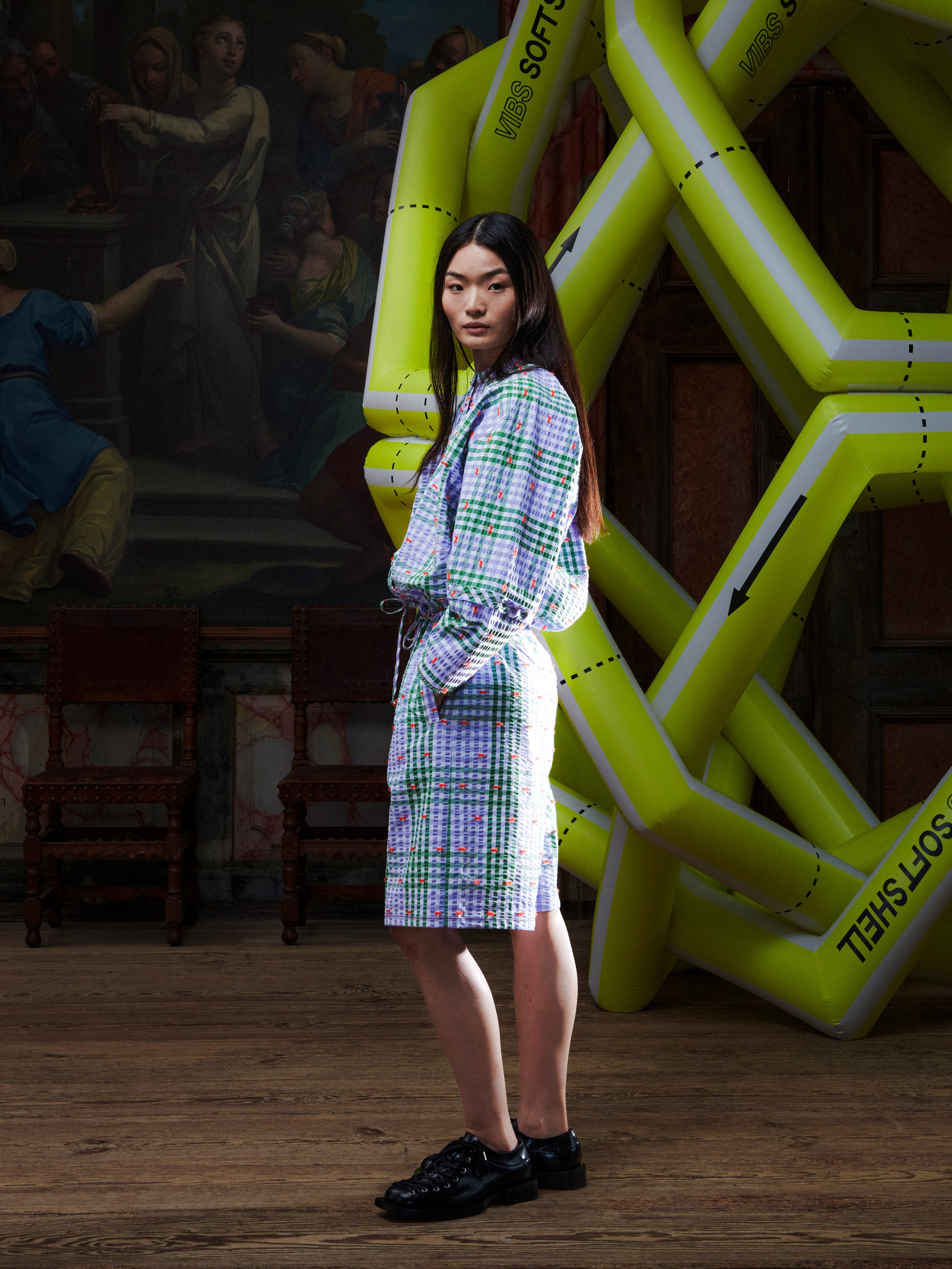 Model wearing the Henrik Vibskov Flat Shirt in Checks Fillé, side view, highlighting the long sleeves, check pattern, and cropped elastic hem.