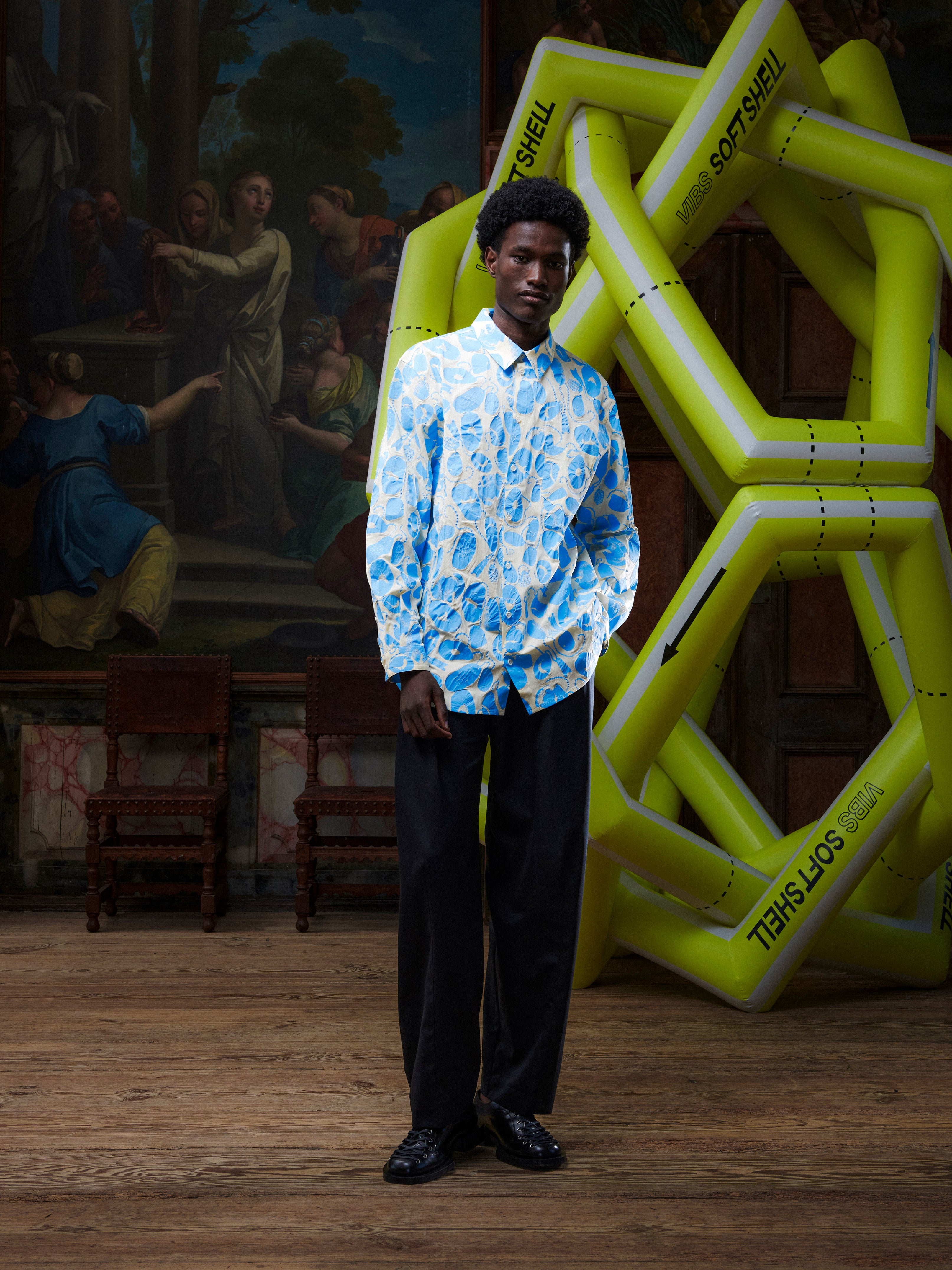 Model wearing the Henrik Vibskov New Blou Shirt in Ecru Amulets, front view. The model is 191 cm and wears size M, showing the off-white shirt with blue amulets pattern, collar, front buttons, and chest pocket.