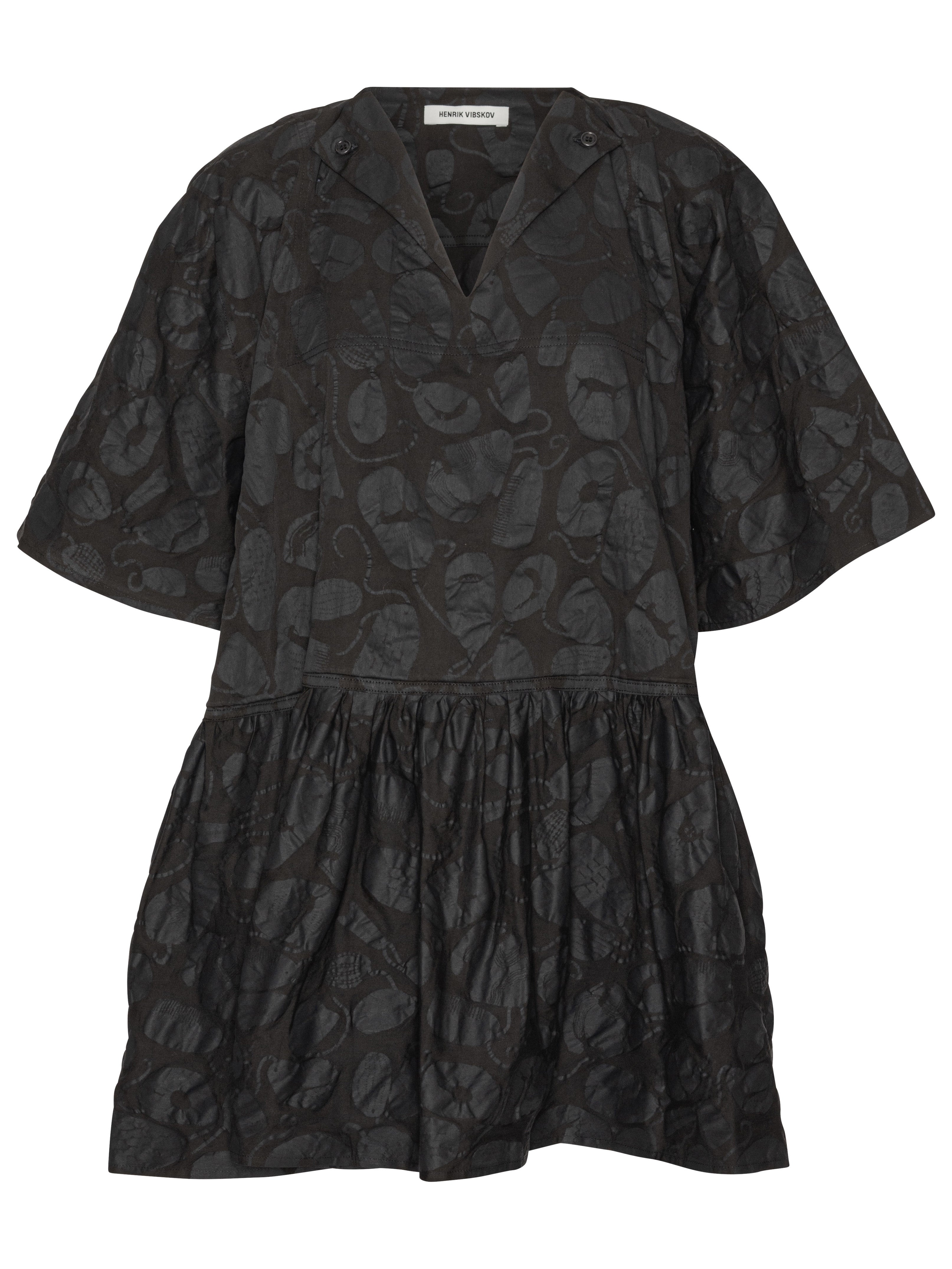 Front view of the Henrik Vibskov Preserve Blouse in Black Amulets, showing the black fabric with amulet pattern, V-neck with button, short sleeves, oversized fit, and wide, knee-length skirt.