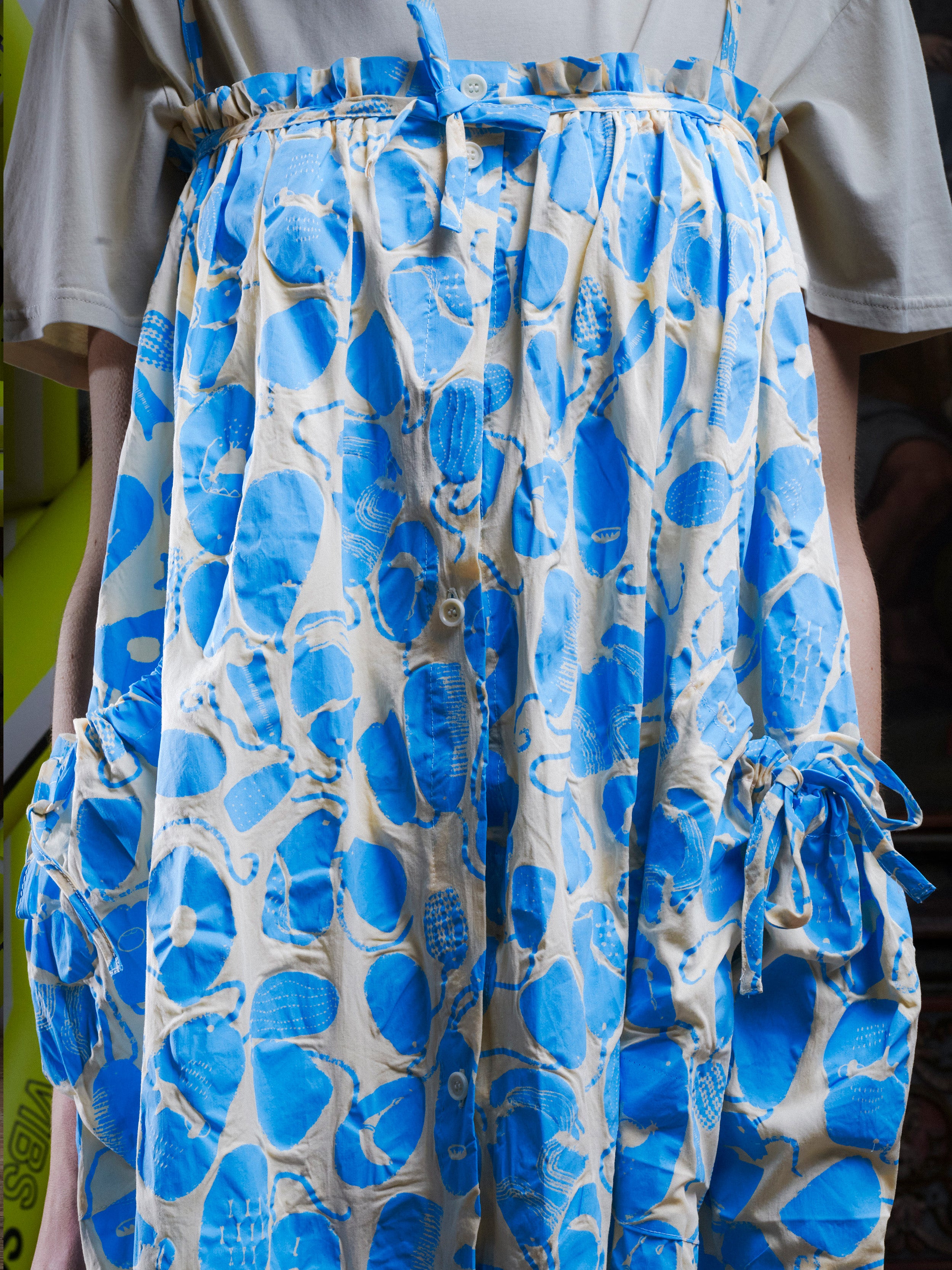 Close-up of a woman wearing the off-white and light blue pattern, sleeveless dress on top of a white t-shirt from Henrik Vibskov.