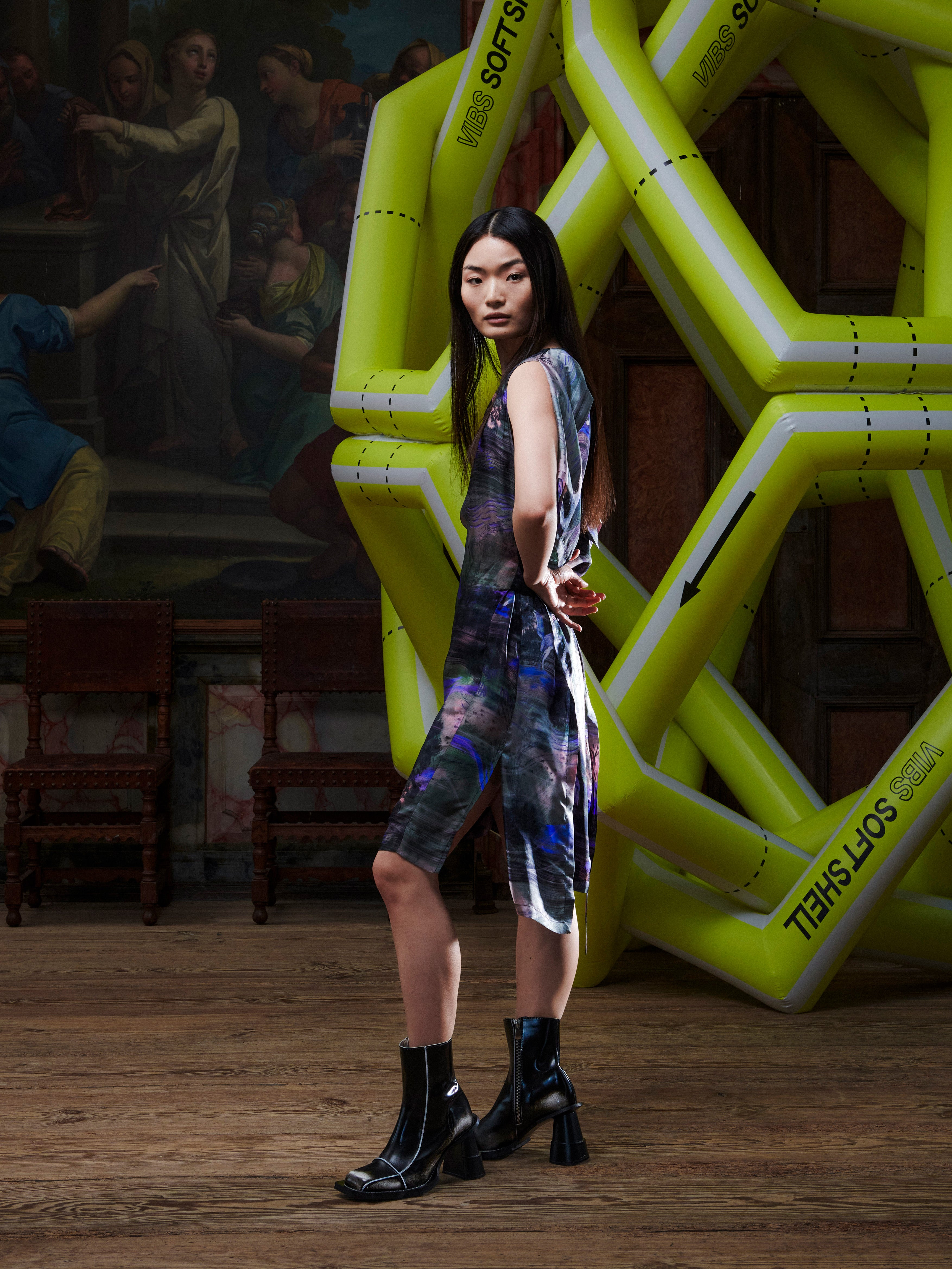 Side profile of woman in a patterned dress standing in front of large inflatable letters in an indoor setting.