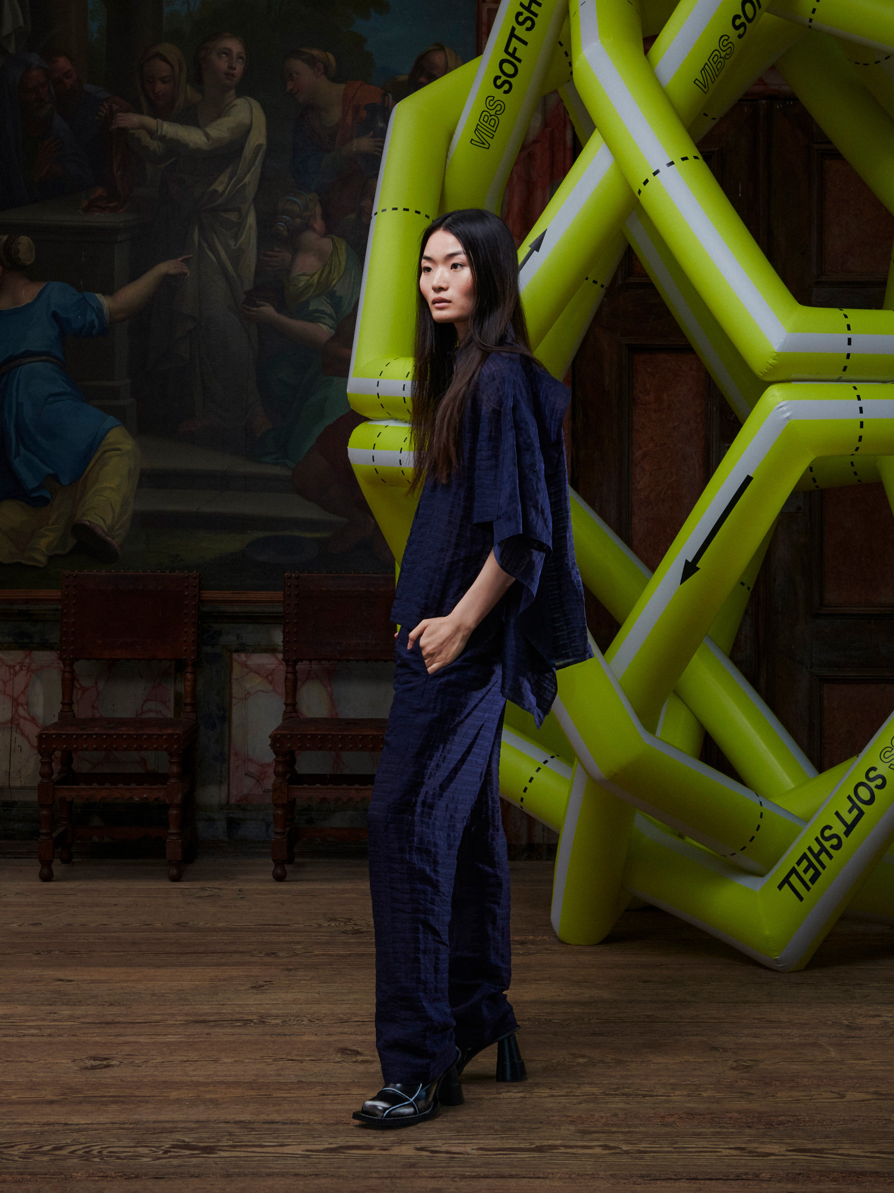 Woman in a dark outfit standing in front of a large yellow inflatable sculpture in an indoor setting.
