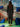 Person wearing a dark outfit standing in front of a tiled wall with abstract patterns and blue sculptures.