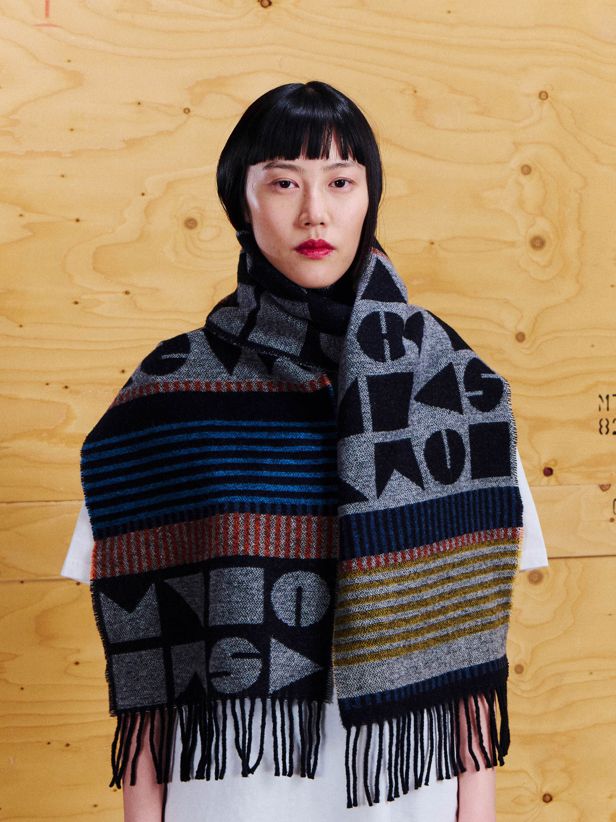 Model wearing the Henrik Vibskov Vibs In Bobs Scarf wrapped around the neck, showing the oversized geometric pattern, striped sections and long fringe.