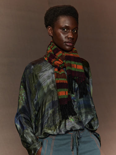 Person wearing a patterned scarf and multicolored shirt against a brown background