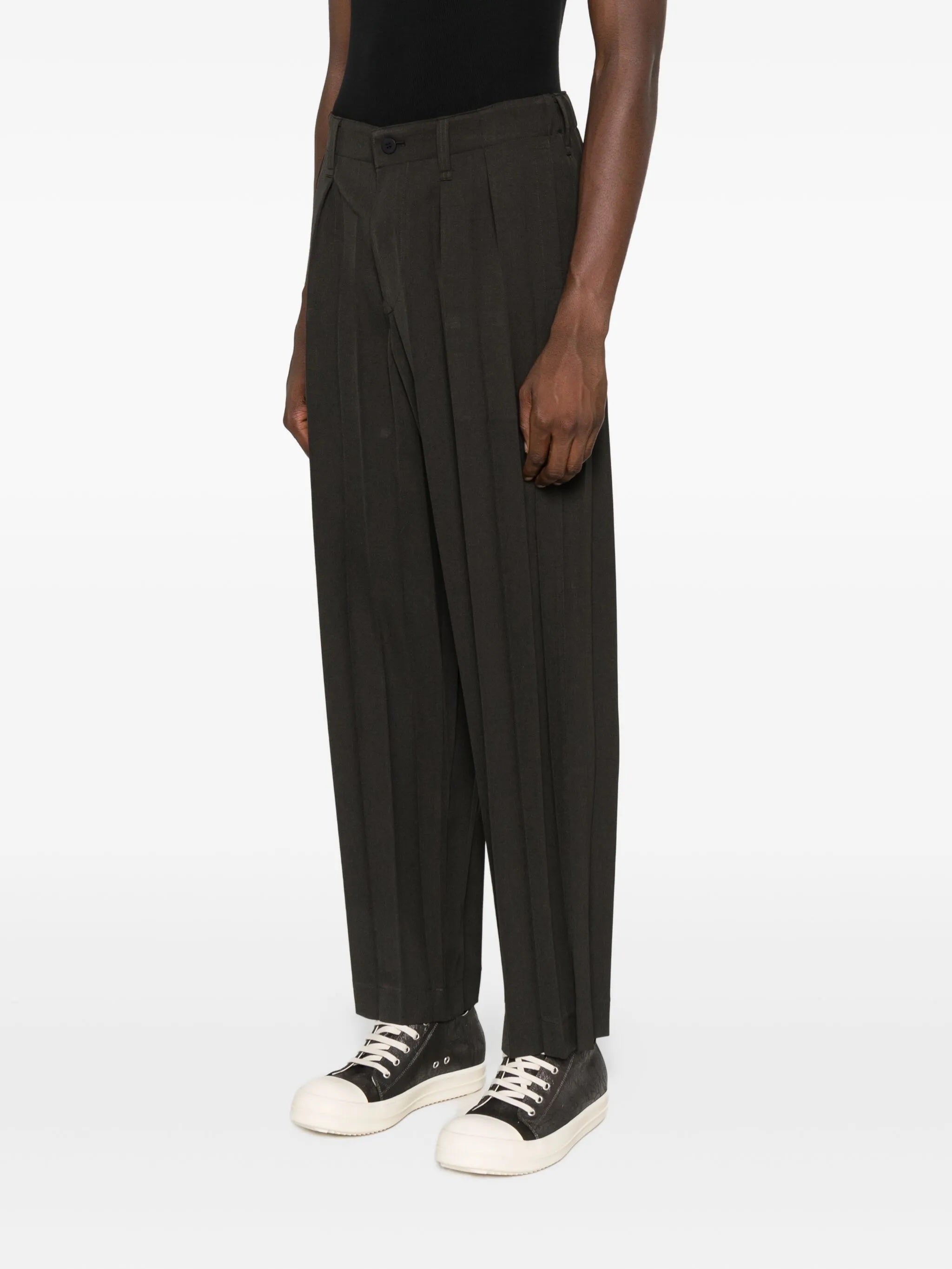 Person wearing dark brown pleated pants with a plain background