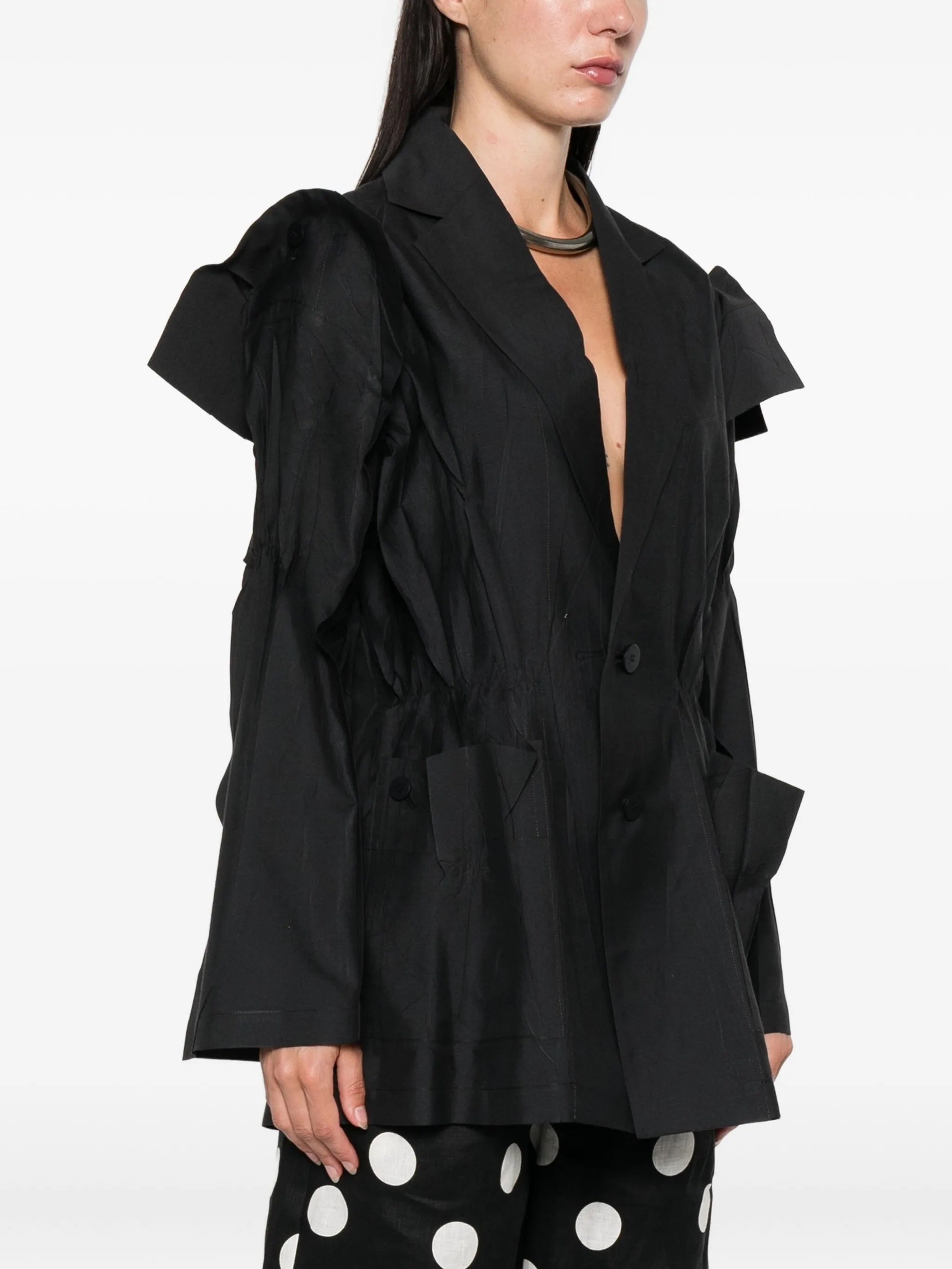 Black blazer with ruffled shoulders worn by a person on a white background