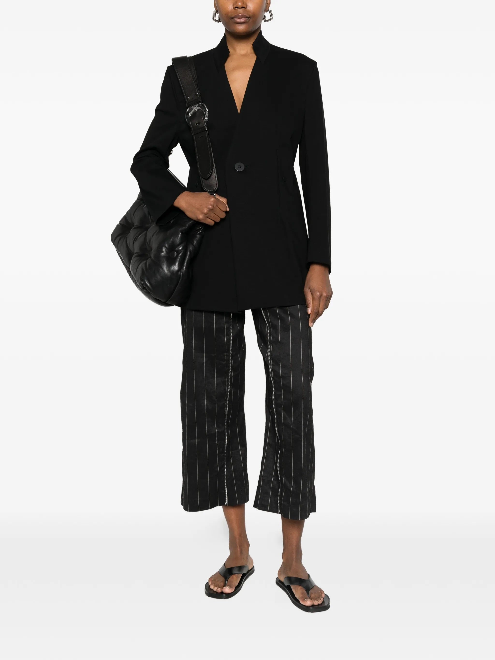 Model wearing the black, single-breasted blazer from Issey Miyake on a white background