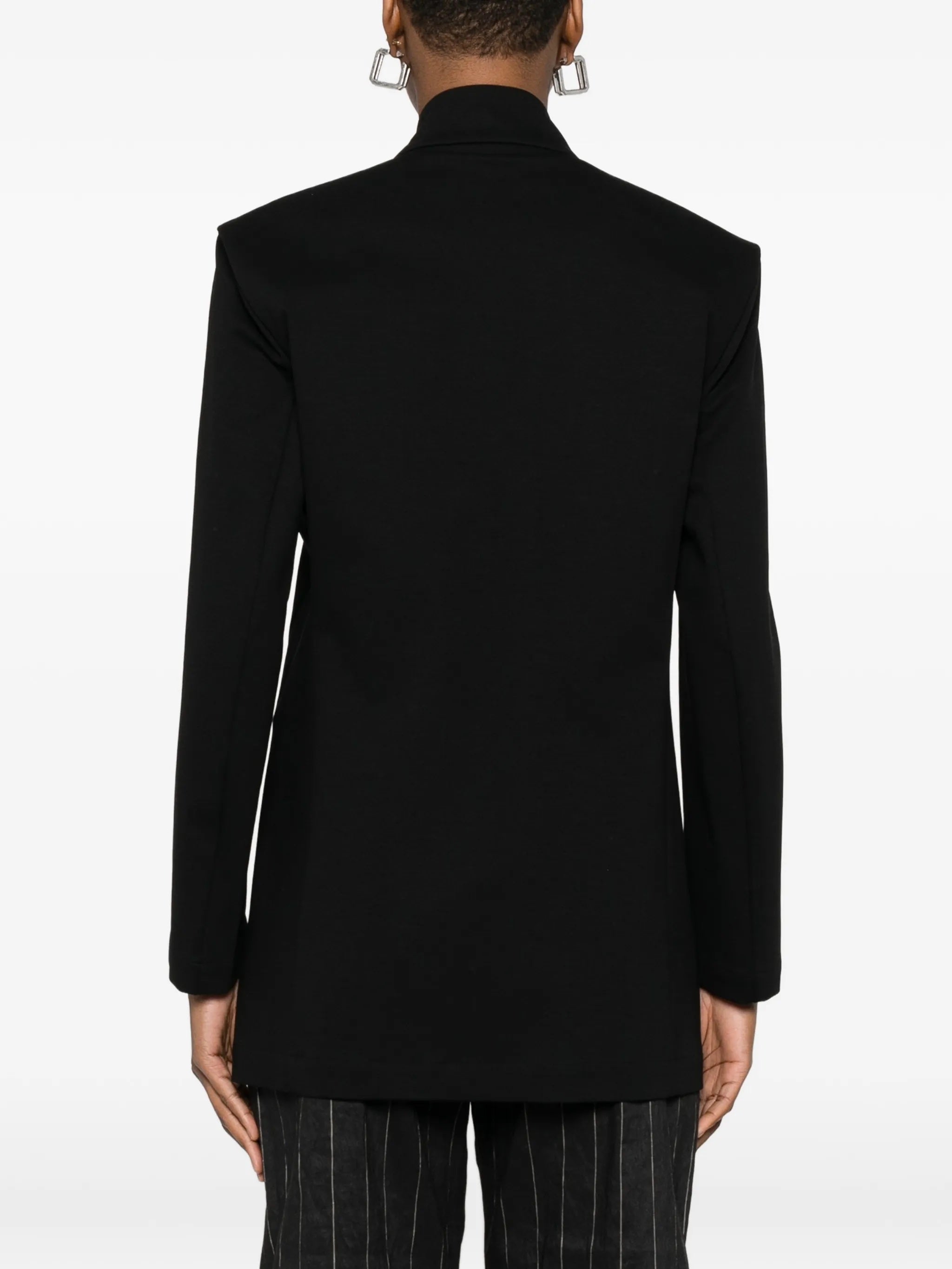 Back view of model wearing the black, single-breasted blazer from Issey Miyake on a white background