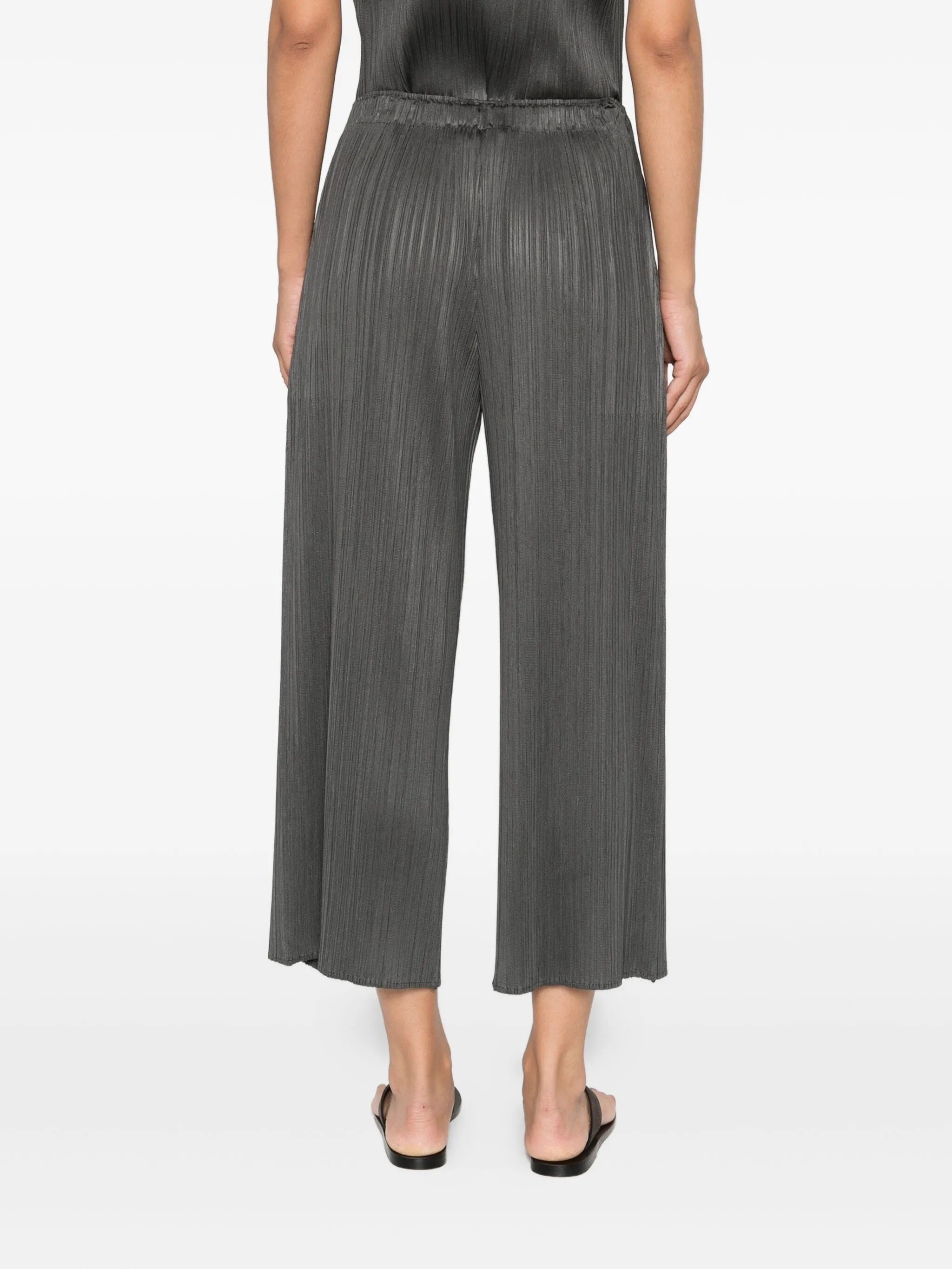 Person wearing gray pleated pants on a white background