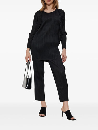 Woman wearing a black pleated outfit from Pleats Please Issey Miyake on a white background