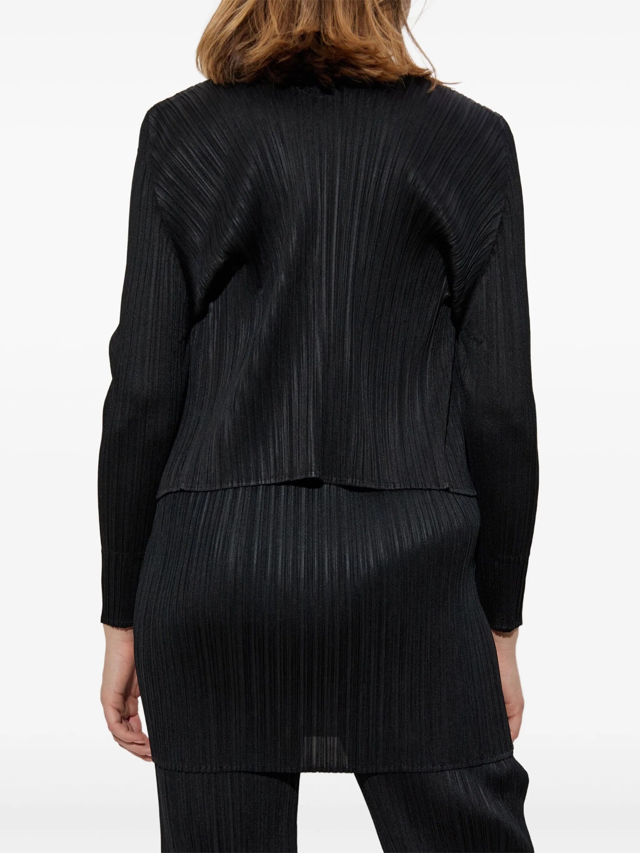 Woman wearing a black pleated outfit from Pleats Please Issey Miyake on a white background