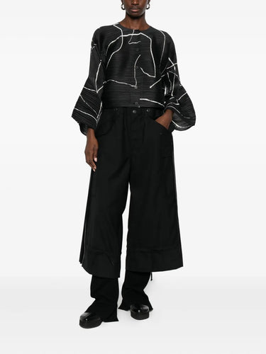 Person wearing a black and white patterned top with wide-leg pants on a white background