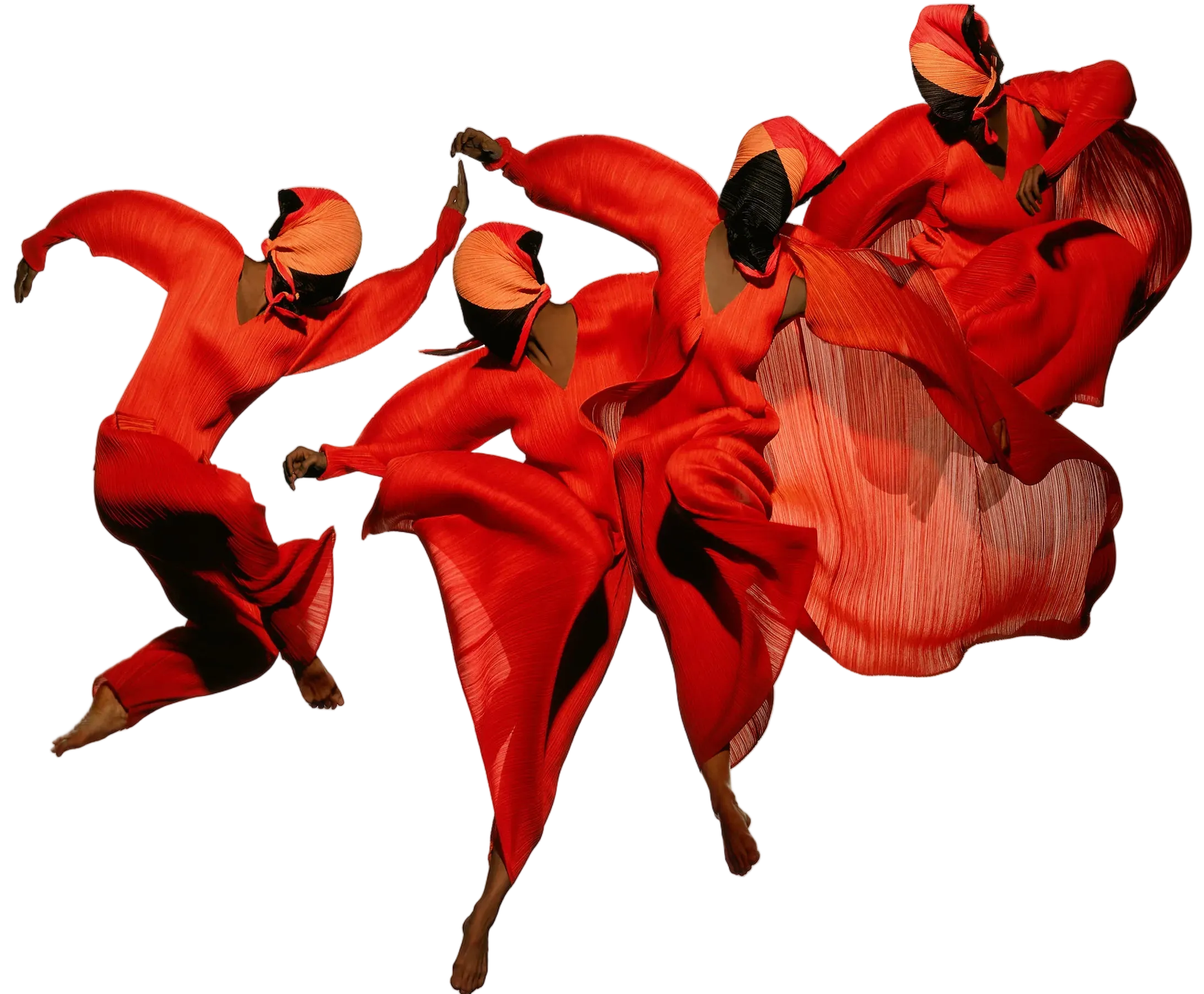 Group of dancers in bright red pleated pleats garments and sculptural headpieces, captured mid-movement against a light background.