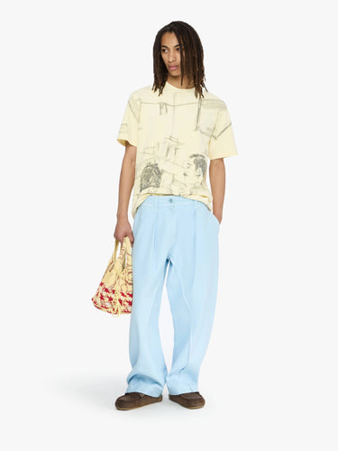 Person wearing a light-colored t-shirt and light blue pants, holding a patterned bag on a white background