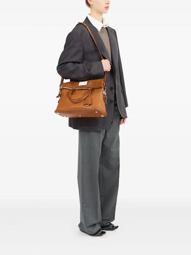 Person carrying a brown 5AC leather bag from Maison Margiela on a white background.