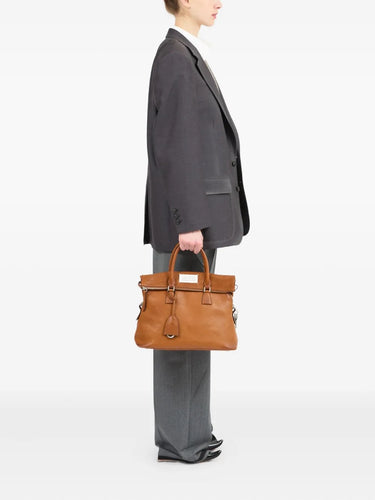 Person carrying a brown 5AC leather bag from Maison Margiela on a white background.