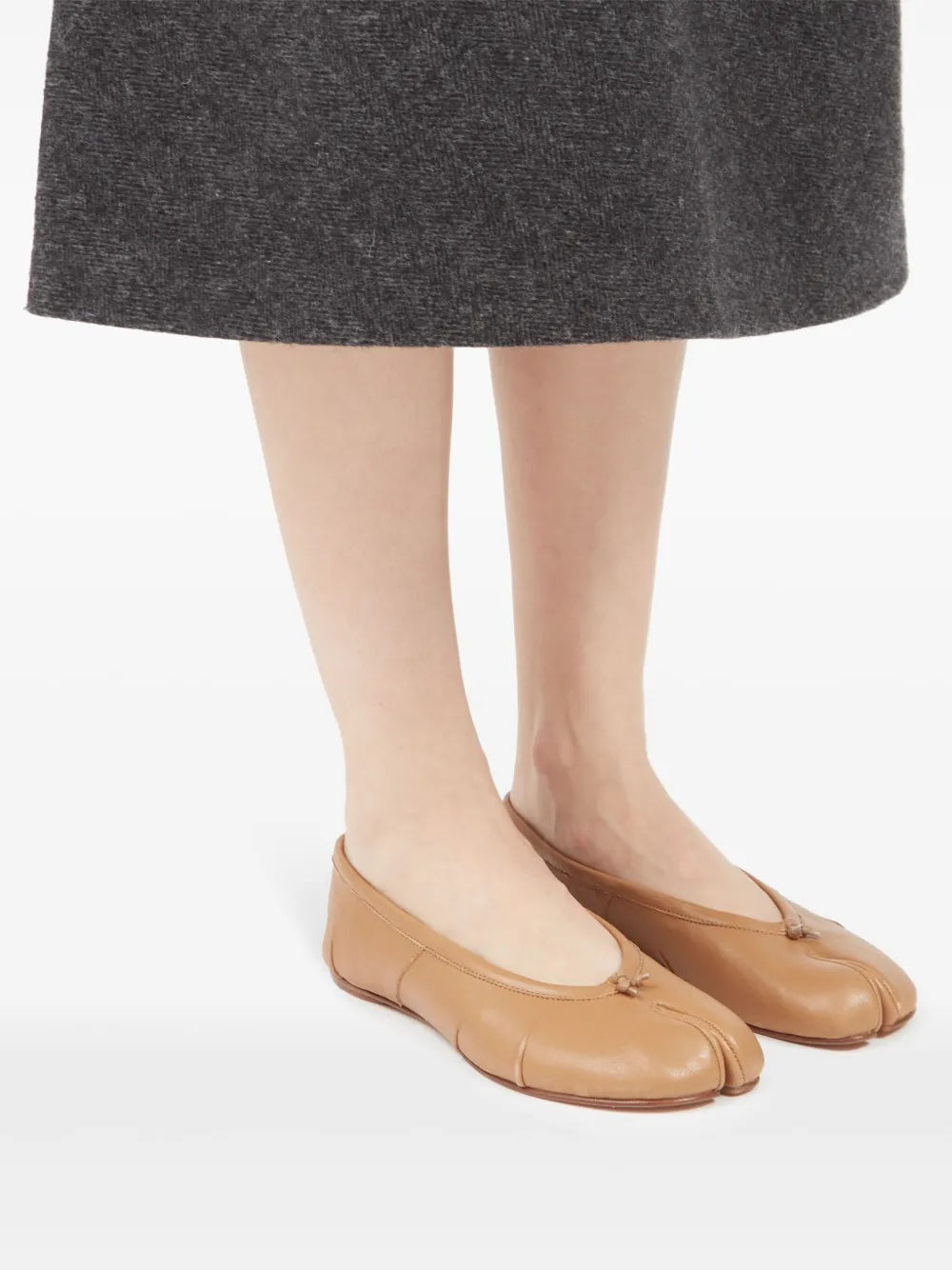 Tan ballet flats worn with a gray skirt on a white background
