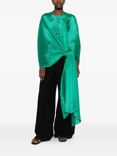 Model wearing the green pleated top called Madam T by Pleats Please Issey Miyake on a white background
