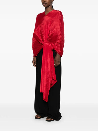 Side view of a model wearing the red pleated top called Madam T by Pleats Please Issey Miyake on a white background