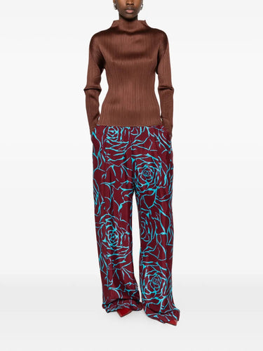 Model wearing the brown, long sleeve, pleated top by Pleats Please Issey Miyake on a white background