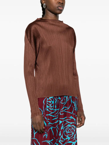 Side view of a model wearing the brown, long sleeve, pleated top by Pleats Please Issey Miyake on a white background