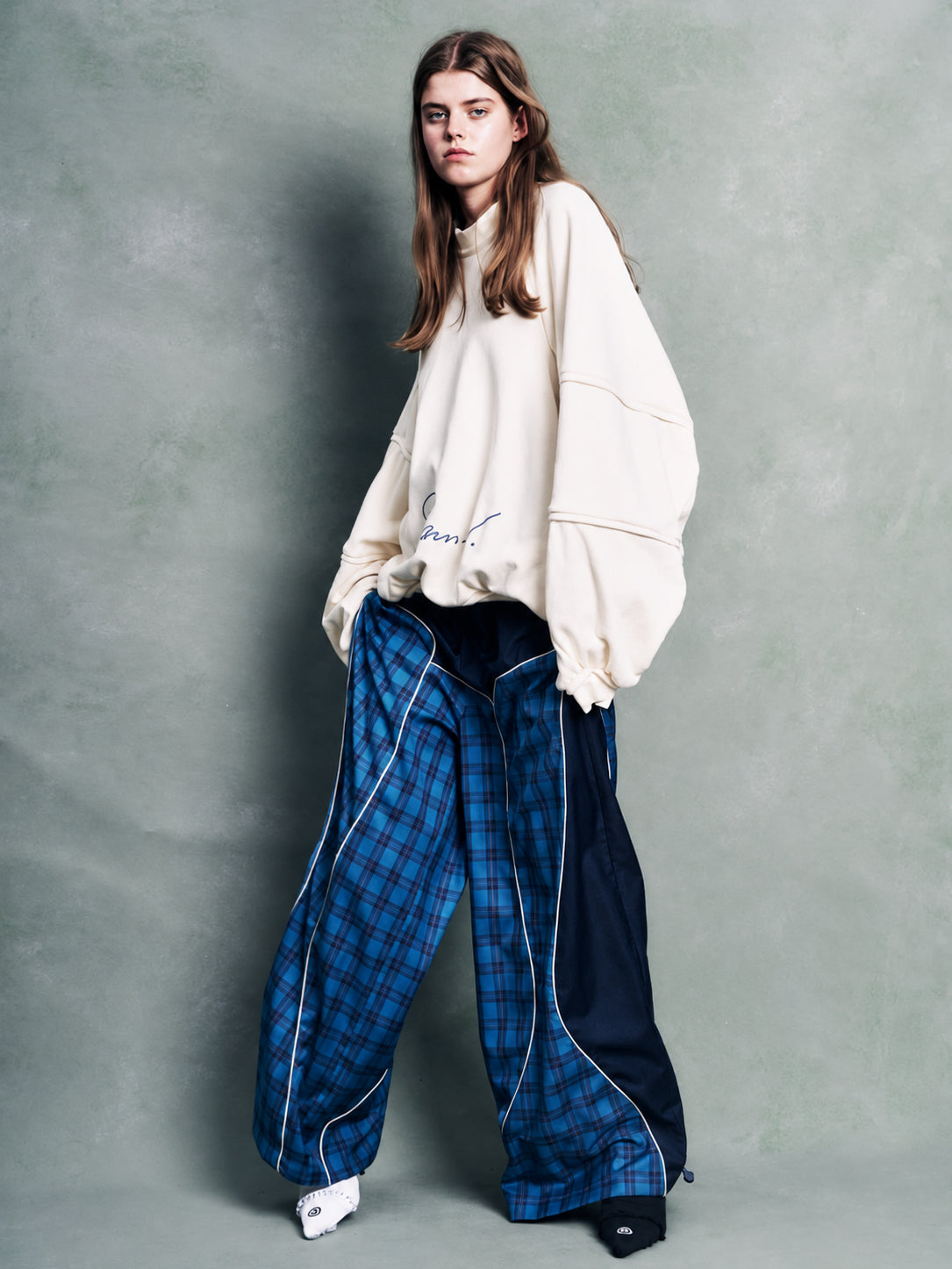 Stamm Exchange Center Check Pants in Blue Check worn with an oversized cream sweatshirt, featuring a wide-leg silhouette, blue check panels, contrasting navy sections and curved white piping details.