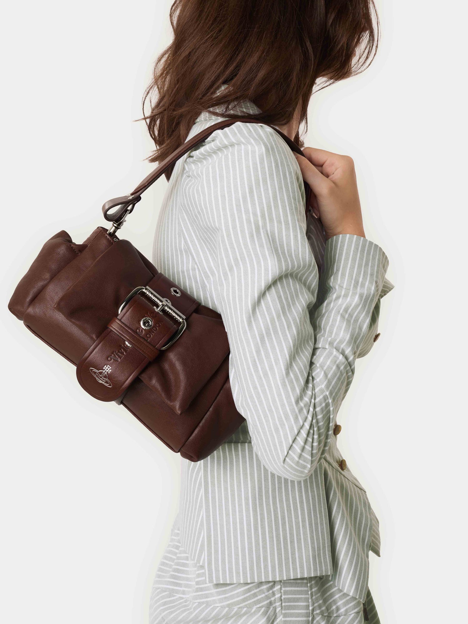 Model wearing Vivienne Westwood Hazel Treasure Handbag in chestnut brown leather on the shoulder with removable chain strap and ruched shape