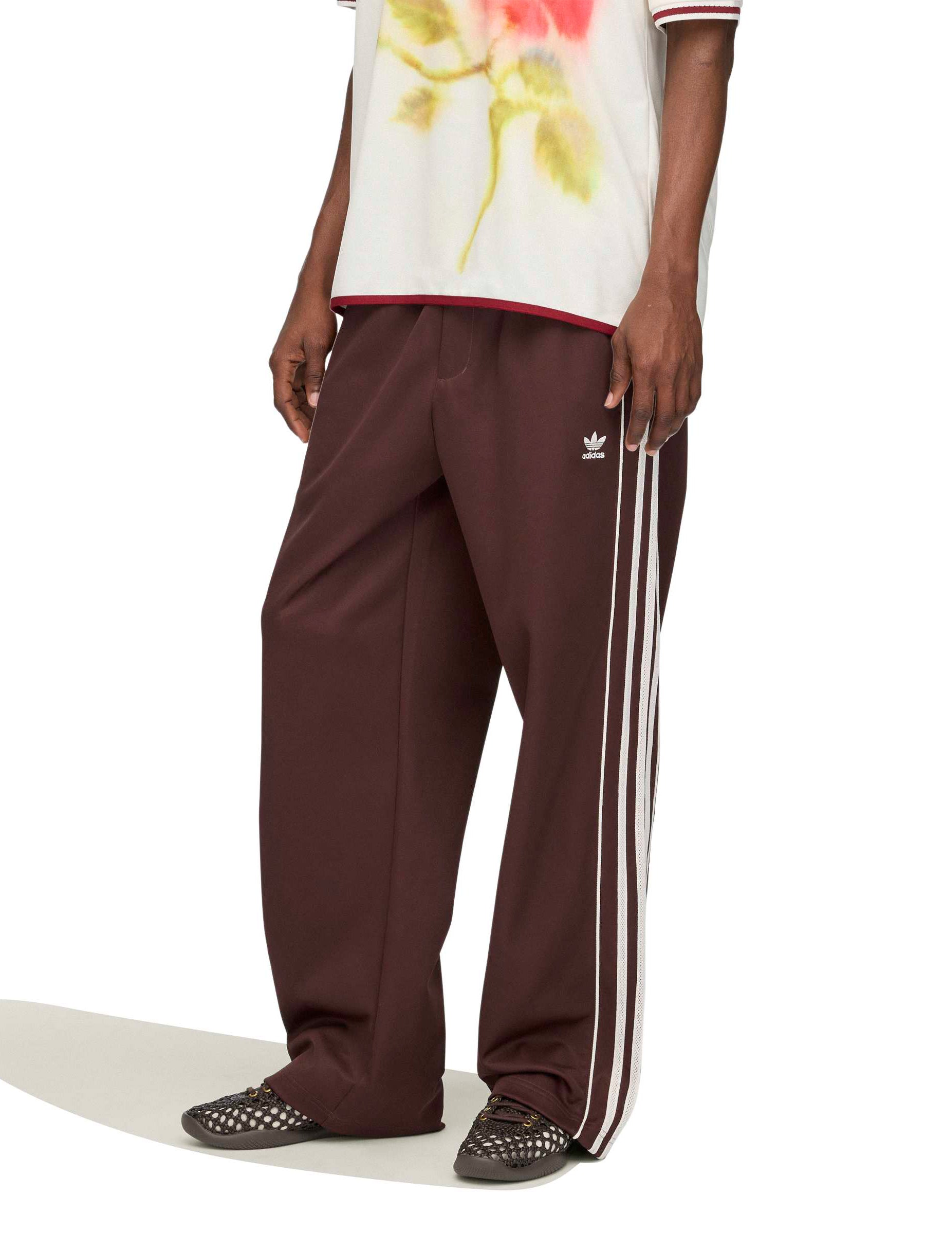 Model wearing the Wales Bonner x Adidas Track Pants in Shadow Brown shadow brown wide-leg track pants with white three-stripe detail, full length side view – Wales Bonner x Adidas SS26