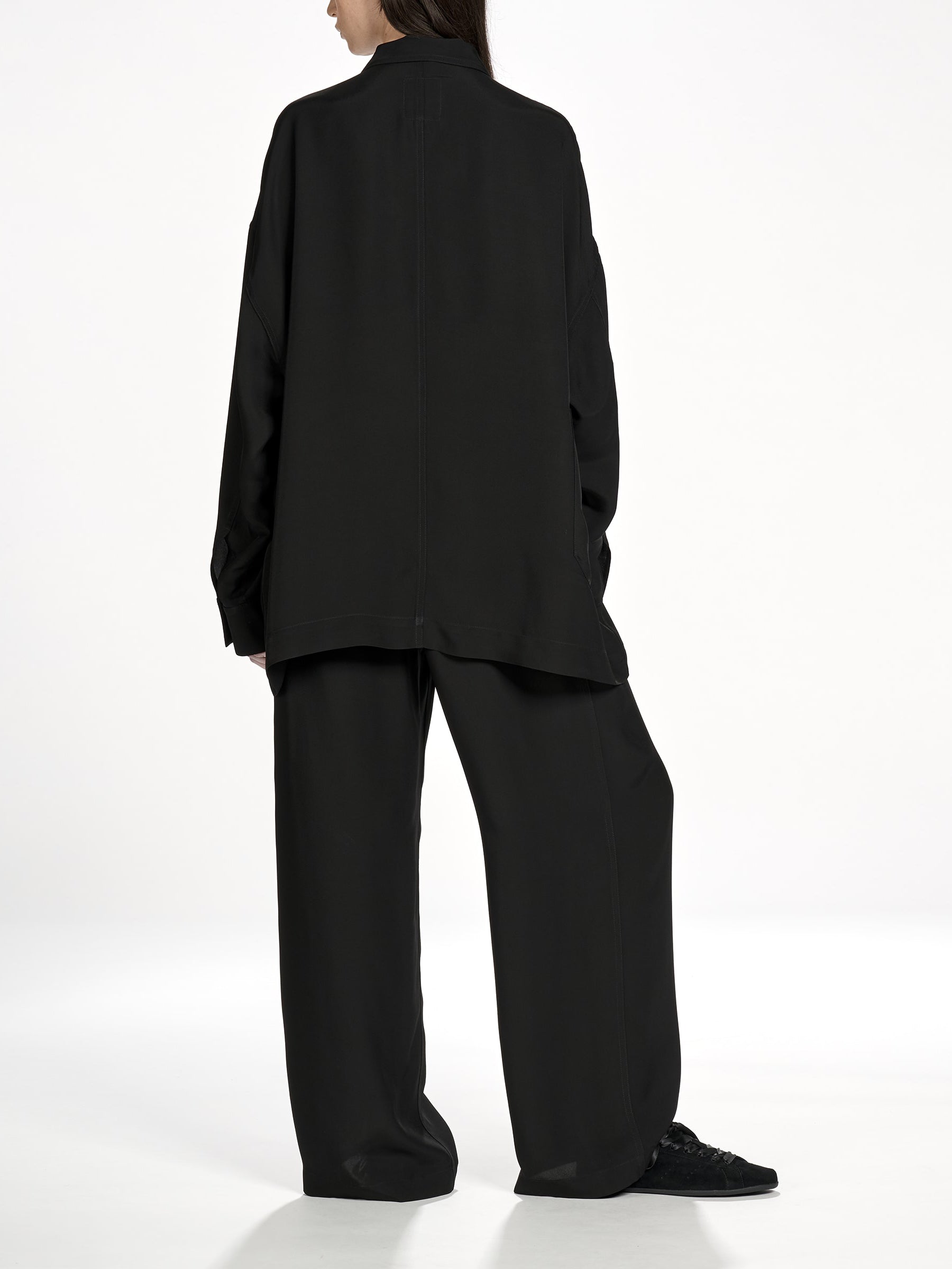 Back view of a female model wearing the Y-3 Chore Jacket Shirt in Black, highlighting the straight hem and loose fit silhouette.