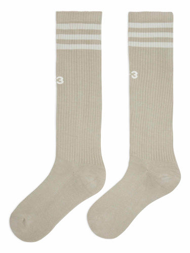 Front packshot of the Y-3 Stripes High Socks in Light Brown, showing the knee-high, high-calf design, engineered 3-Stripes cuff, and embroidered Y-3 logo at the centre front.
