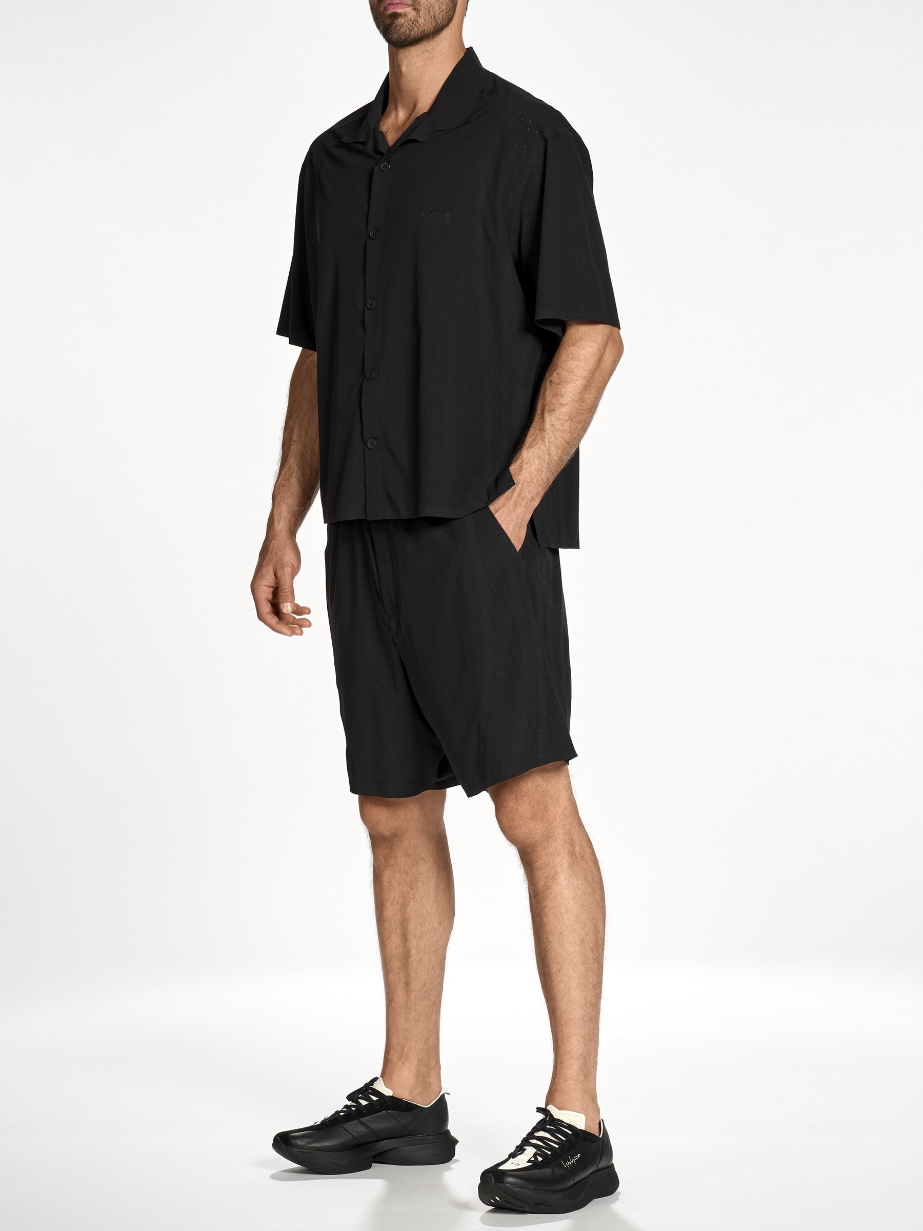 Side view of a male model wearing the Y-3 Ultralight Woven Shirt in Black, emphasizing the stretch woven fabric, short sleeves, and bonded ventilation slits.