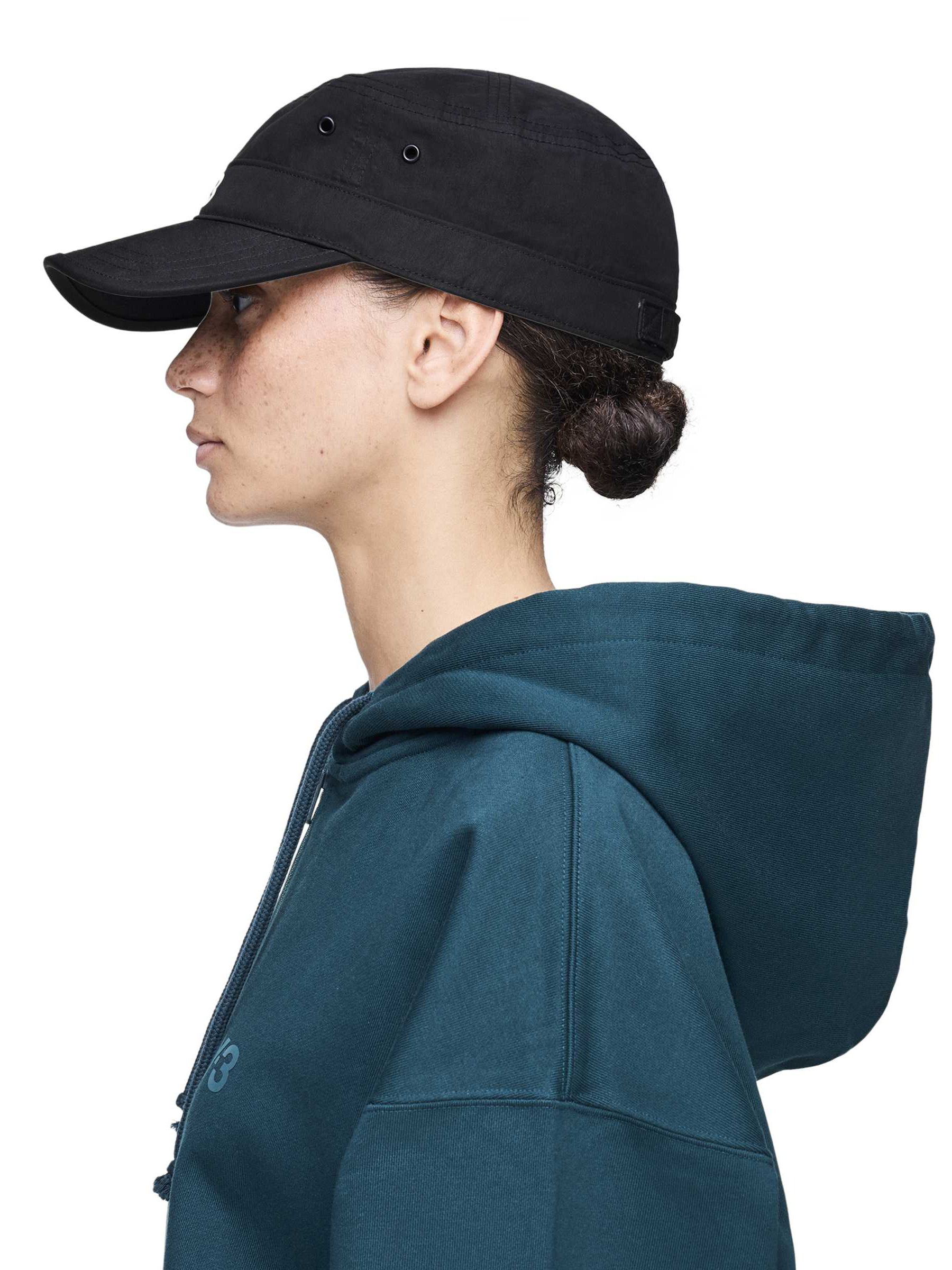 Side view of a female model wearing the Y-3 Workwear Cap in Black, showing the curved brim, structured fit, and silicone Y-3 logo at the front.