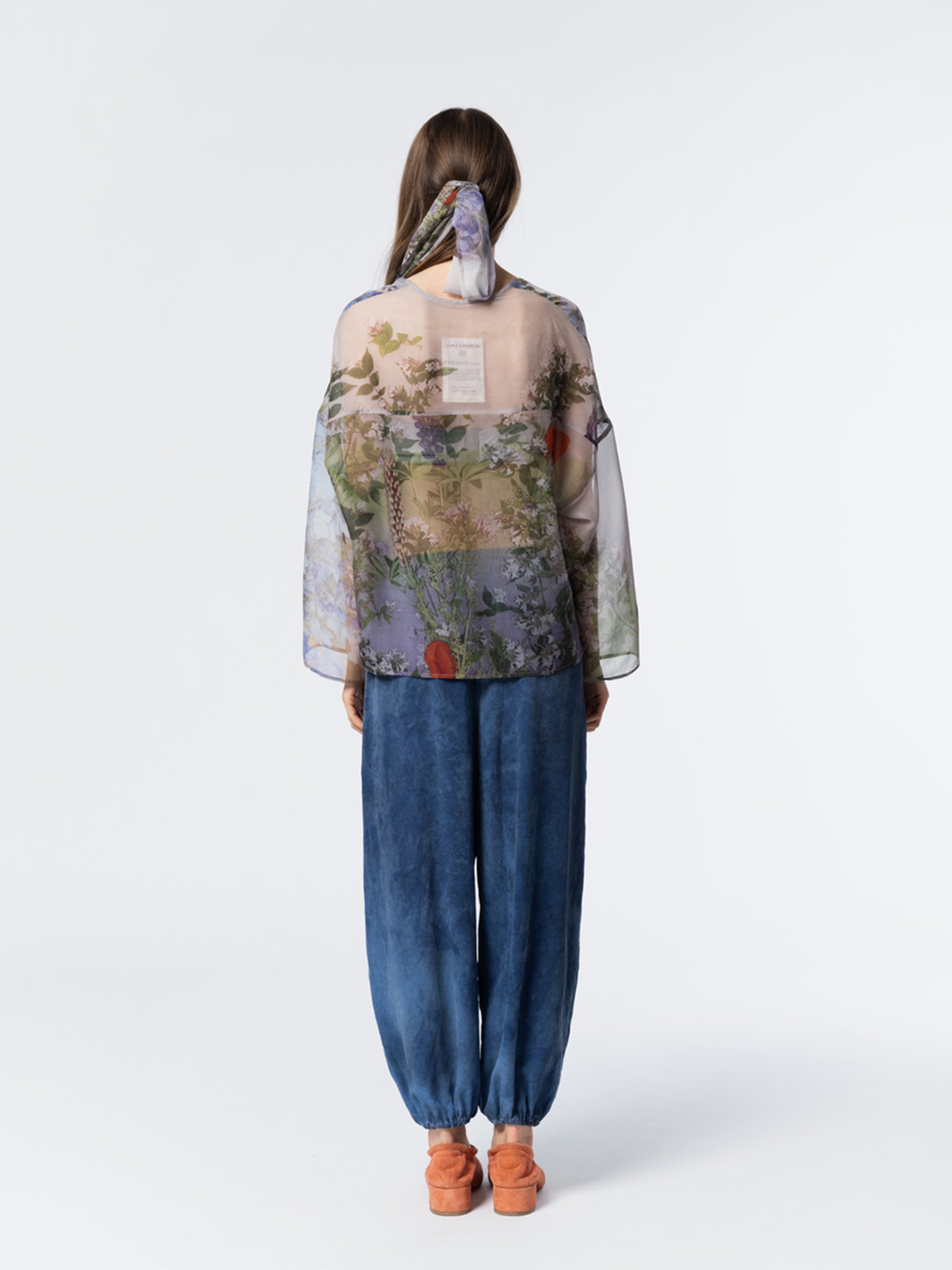 Back view of model wearing the Anntian Chiffon Silksweater in Print R, a loose-fit semi see-through chiffon sweater in a multicolour floral print with blue tones and long sleeves
