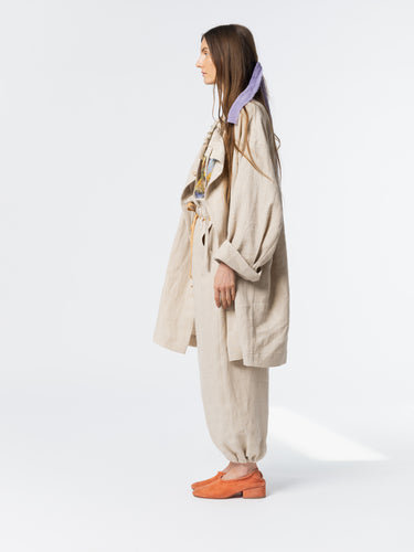 Side view of model wearing the Anntian Trench Jacket Hemp in Natural, highlighting the loose silhouette and adjustable drawstring neckline in off-white hemp