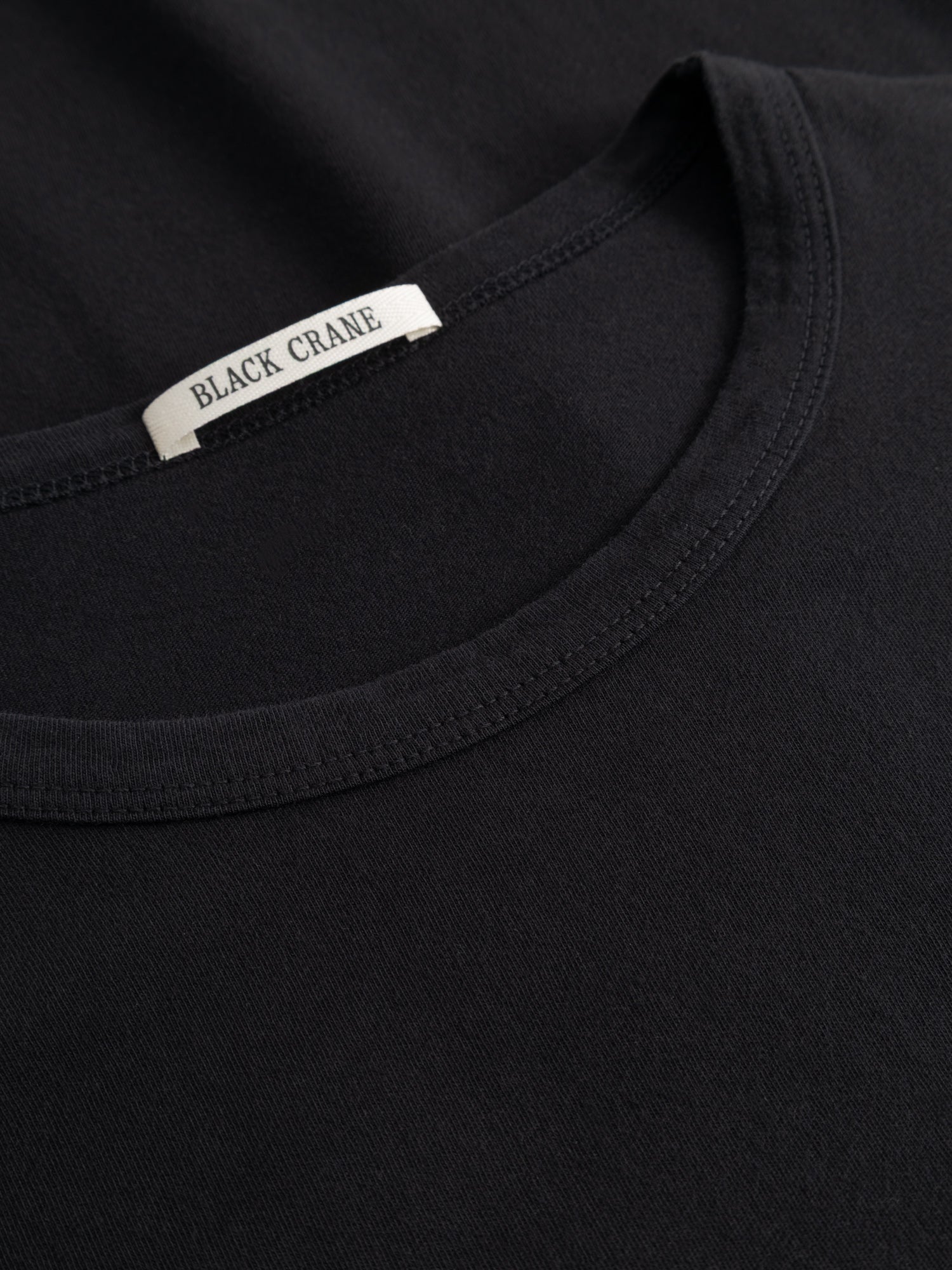 Close-up of the Black Crane black longsleeve tee showing the fabric texture and brand label at the neckline.