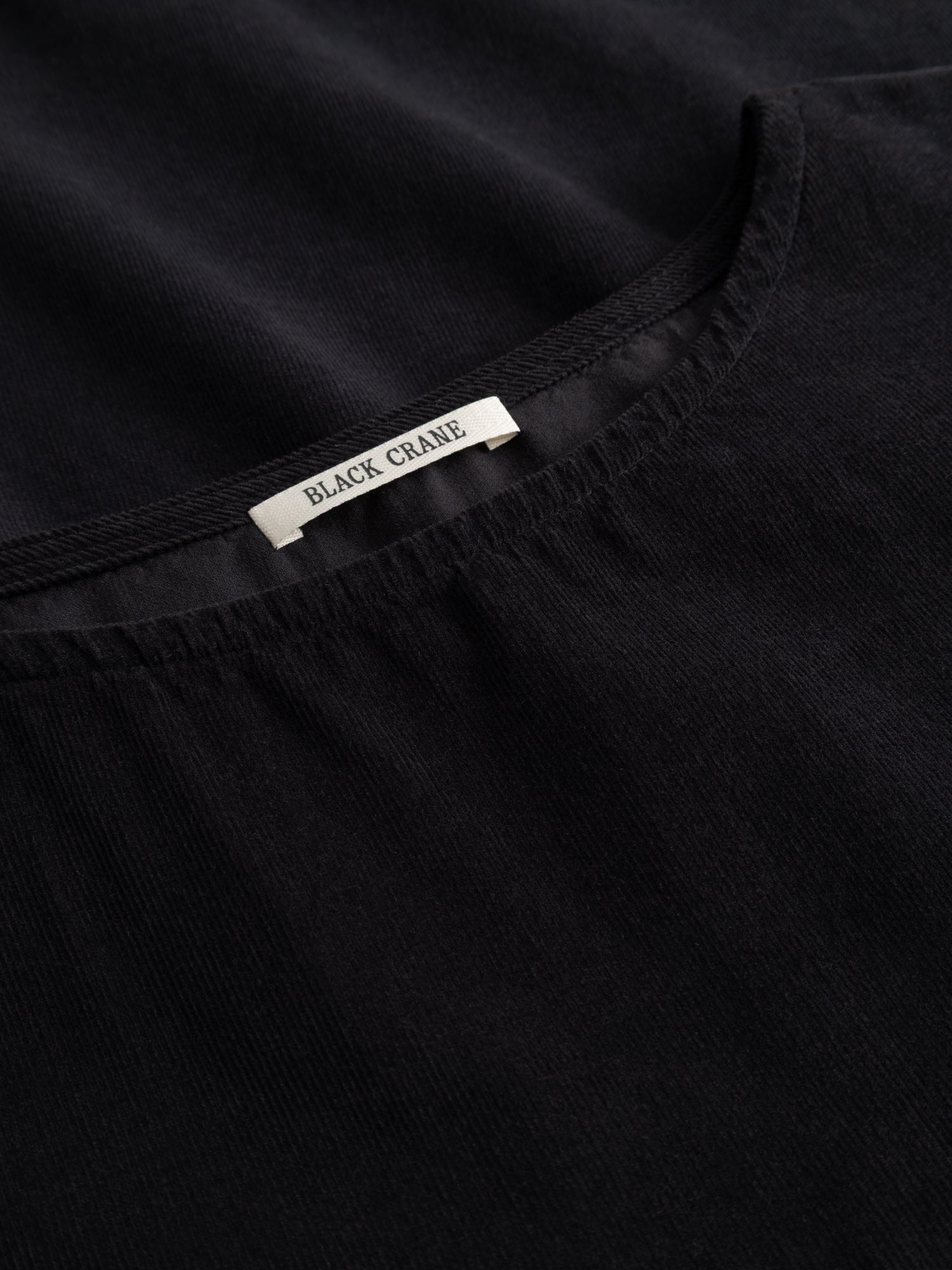 Close-up of the Black Crane Painter Dress showing the dark navy corduroy texture and the brand label at the neckline.